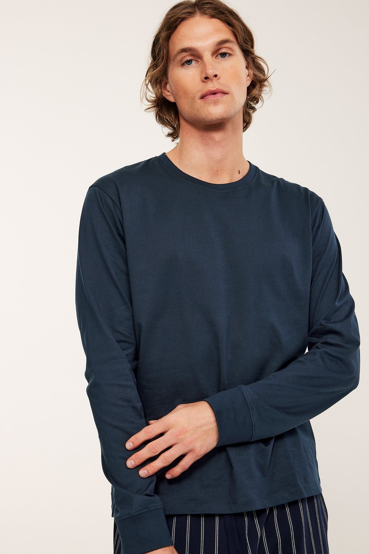 Widok z przodu: mężczyzna w granatowej, bawełnianej piżamie z długim rękawem na pasiasznych spodniach.