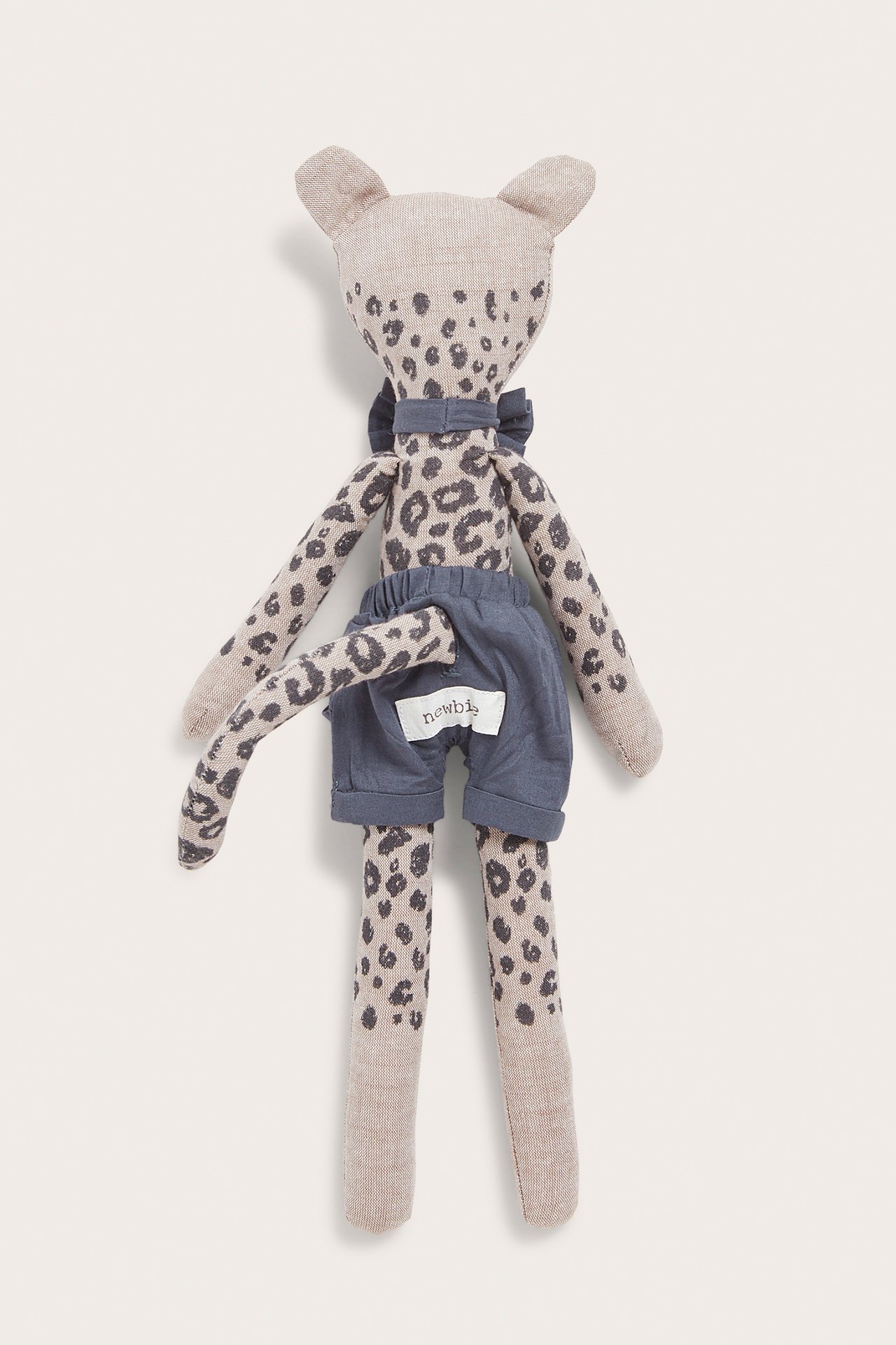 Edestä näkymä beigestä leopardikuvioisesta pehmolelusta, jossa on siniset shortsit ja sininen rusetti.