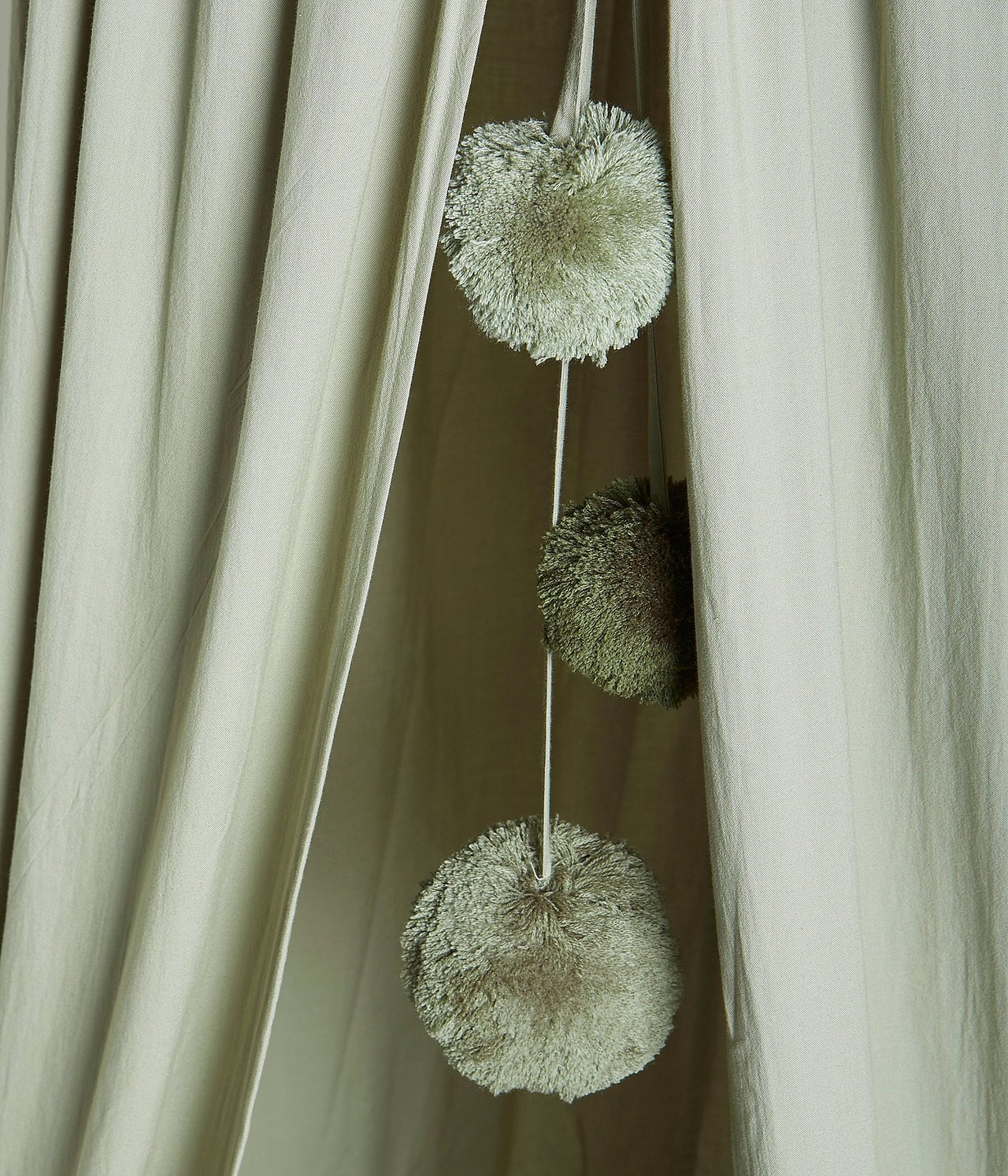 Zbliżenie na ciemnozielony namiot do czytania z trzema wiszącymi pomponami.