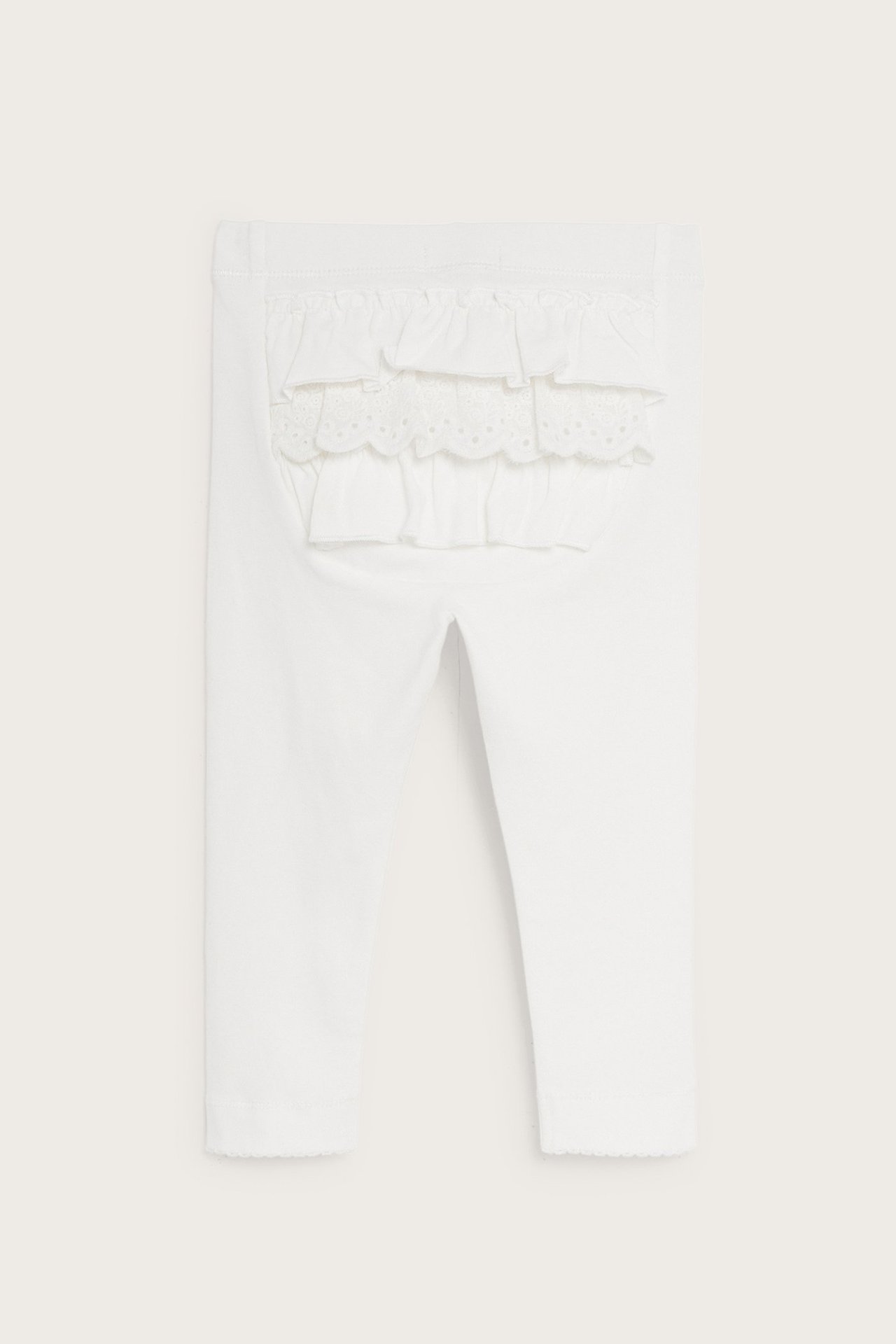 Bakifrån: Offwhite baby leggings med resår i midjan, volanger och spetsdetaljer baktill.