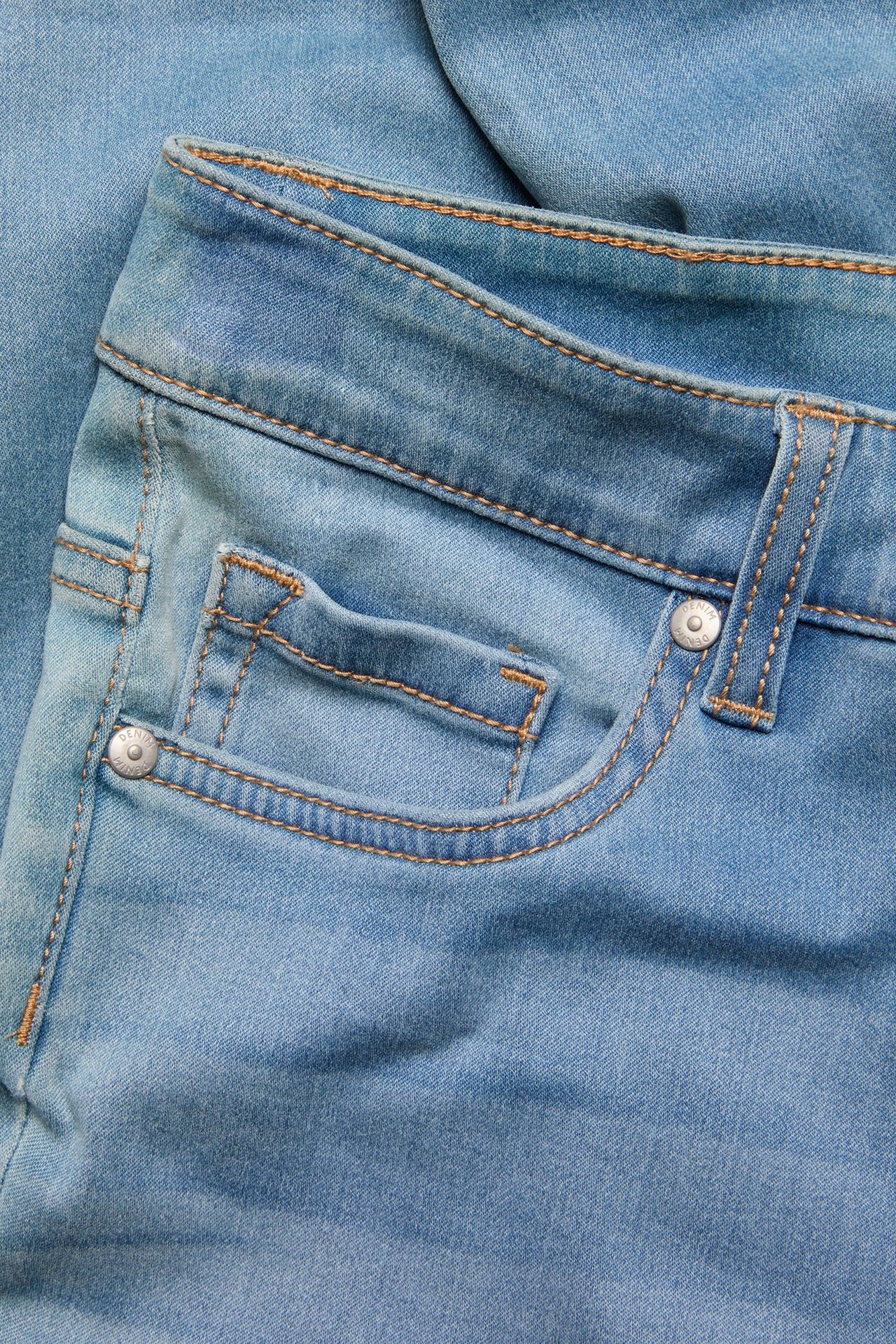 Zbliżenie na jasnoniebieskie dżinsy slim z denimu, pokazujące przednią kieszeń, pas i metalowy nit.