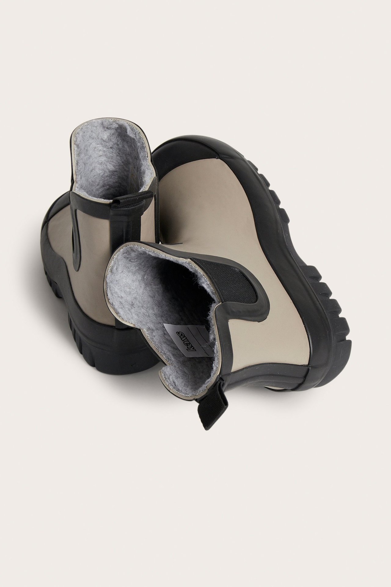 Ylhäältä kuvattu lasten vuoratut mustat ja vaaleanbeiget kumisaappaat harmaalla vuorella.