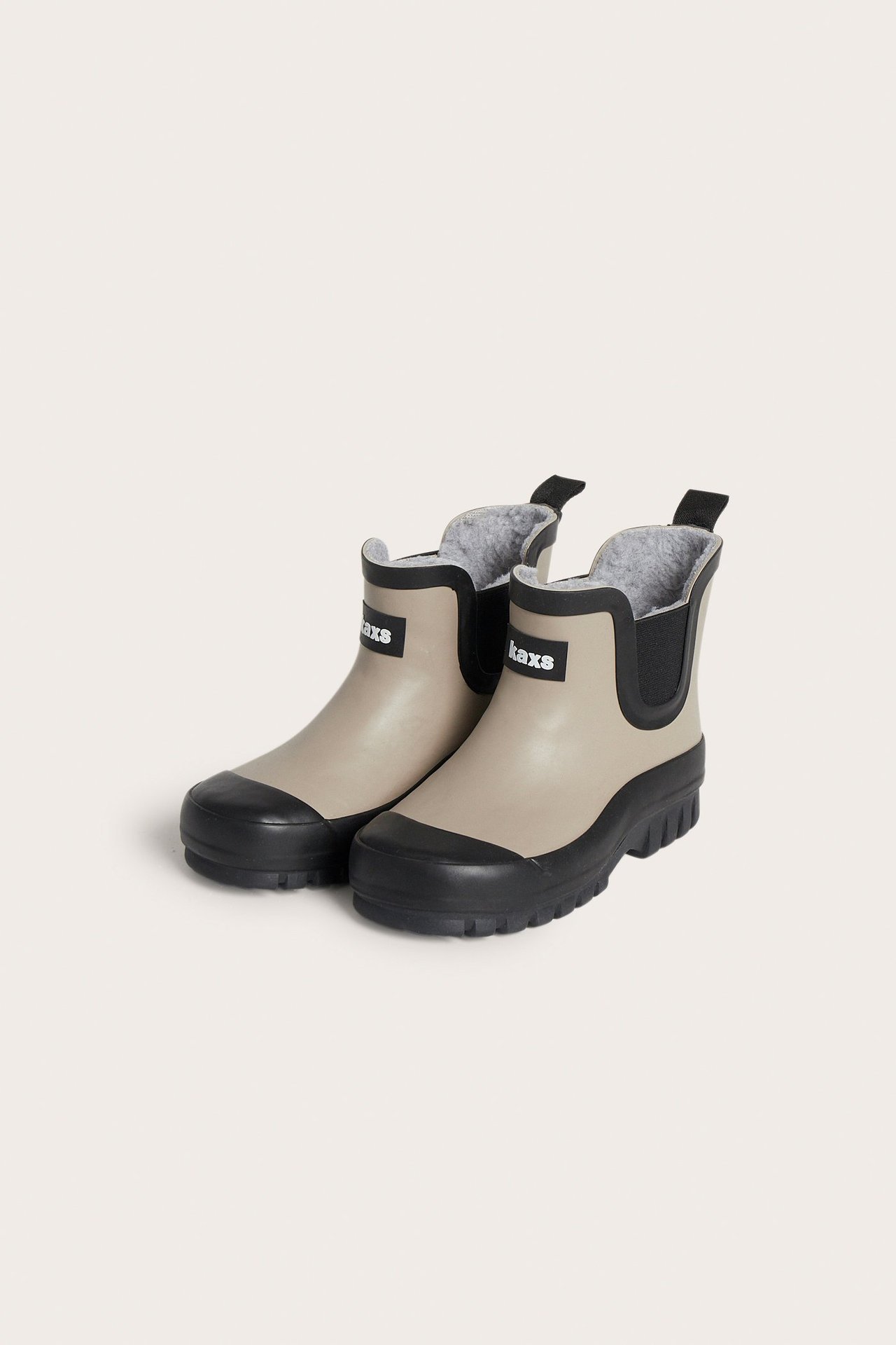 Edestä: beiget vuoratut Chelsea-kumisaappaat mustilla pohjilla, kärjillä, joustosivuilla ja Kaxs-logolla.