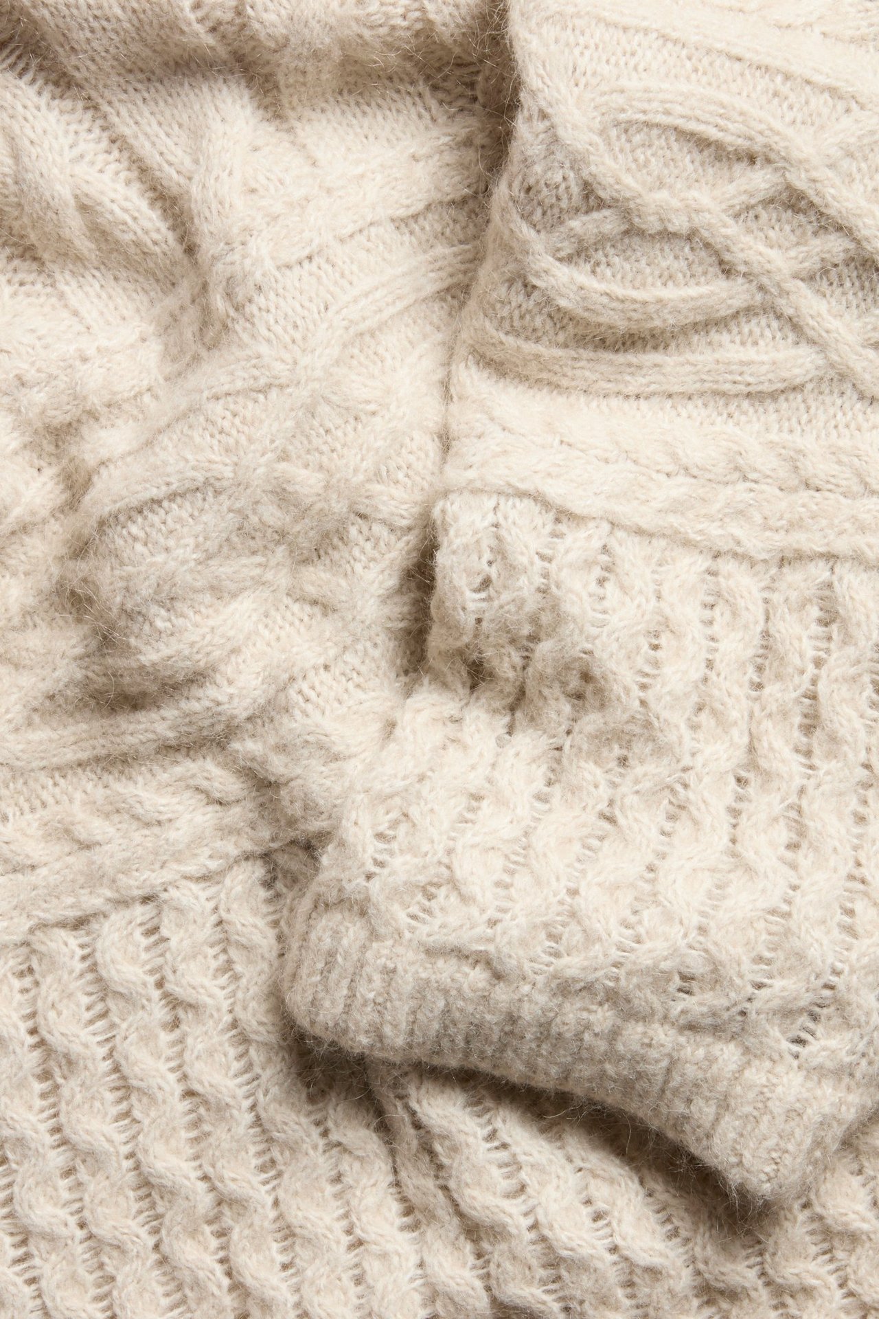 Zbliżenie jasnobeżowego swetra z mieszanki wełny z różnorodnymi wzorami warkoczowymi.