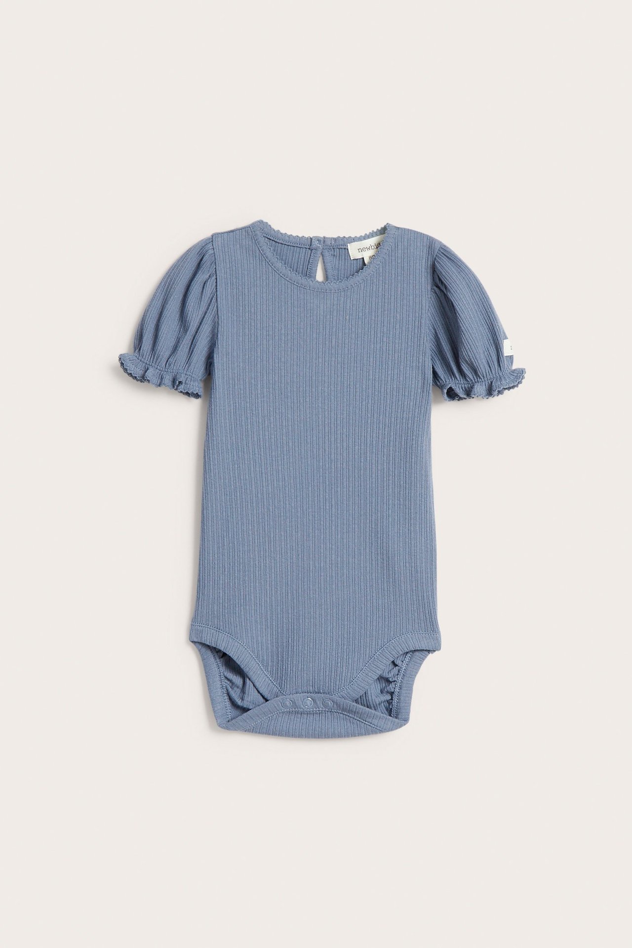 Framsida av en enfärgad blå ribbad jersey babybody med korta puffärmar, picotkant och tryckknappar.