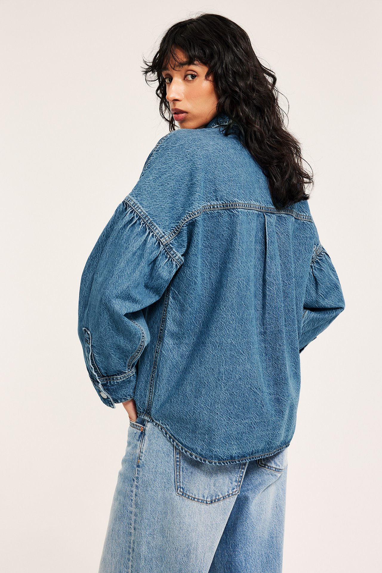 Naisen yllä väljä sininen denimit-paita laskostetuilla hihoilla ja vaaleansiniset leveälahkeiset farkut.