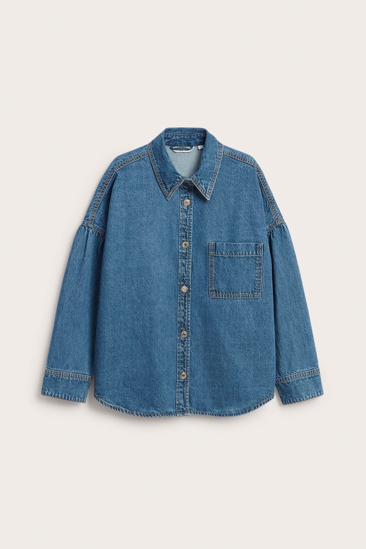 Edestäpäin sininen farkkupaita, jossa laskevat olkapäät, laskostetut hihat, rintatasku ja painonapit.