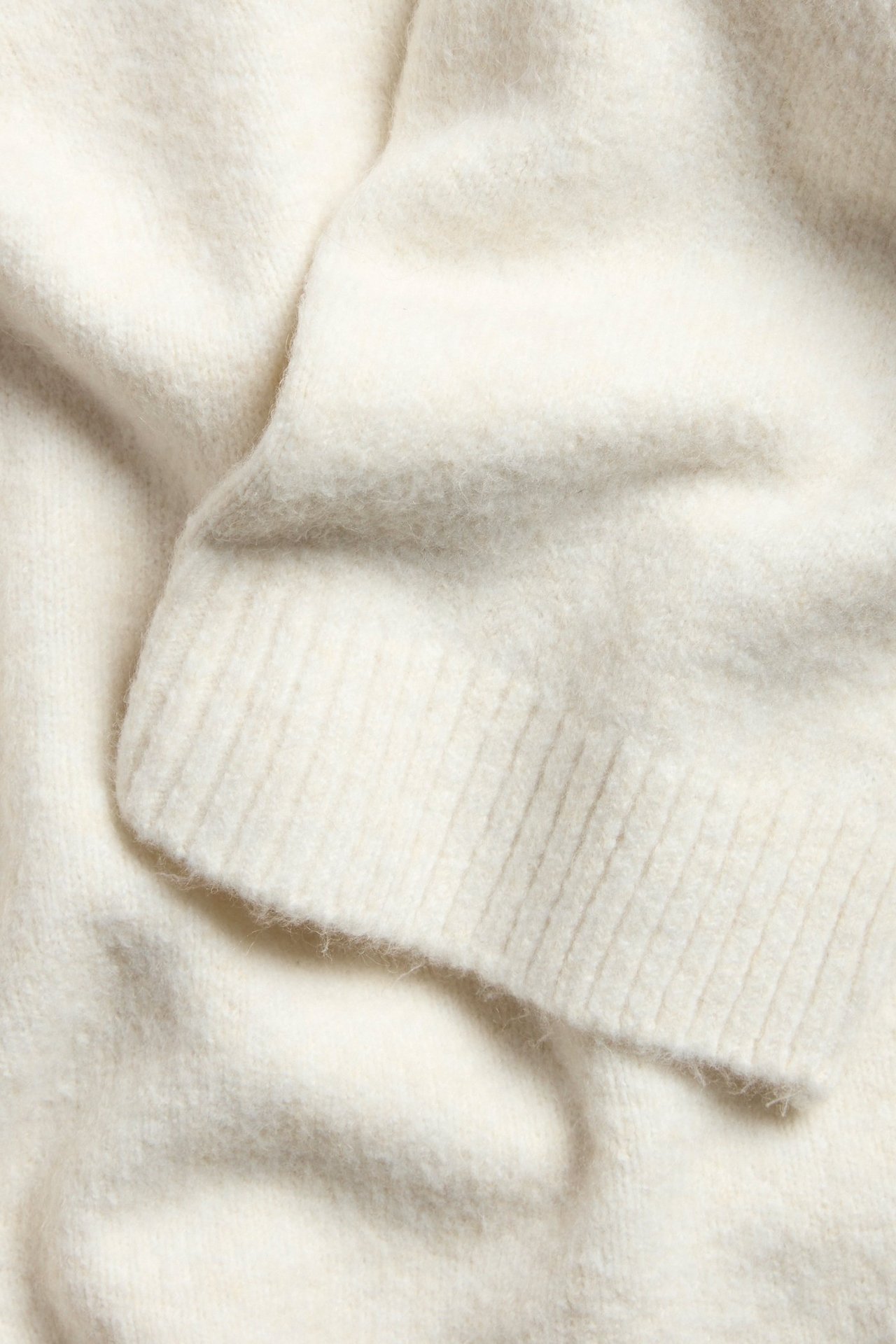 Zbliżenie na biały melanżowy sweter z dzianiny, ukazujące jego miękki materiał i prążkowany mankiet.