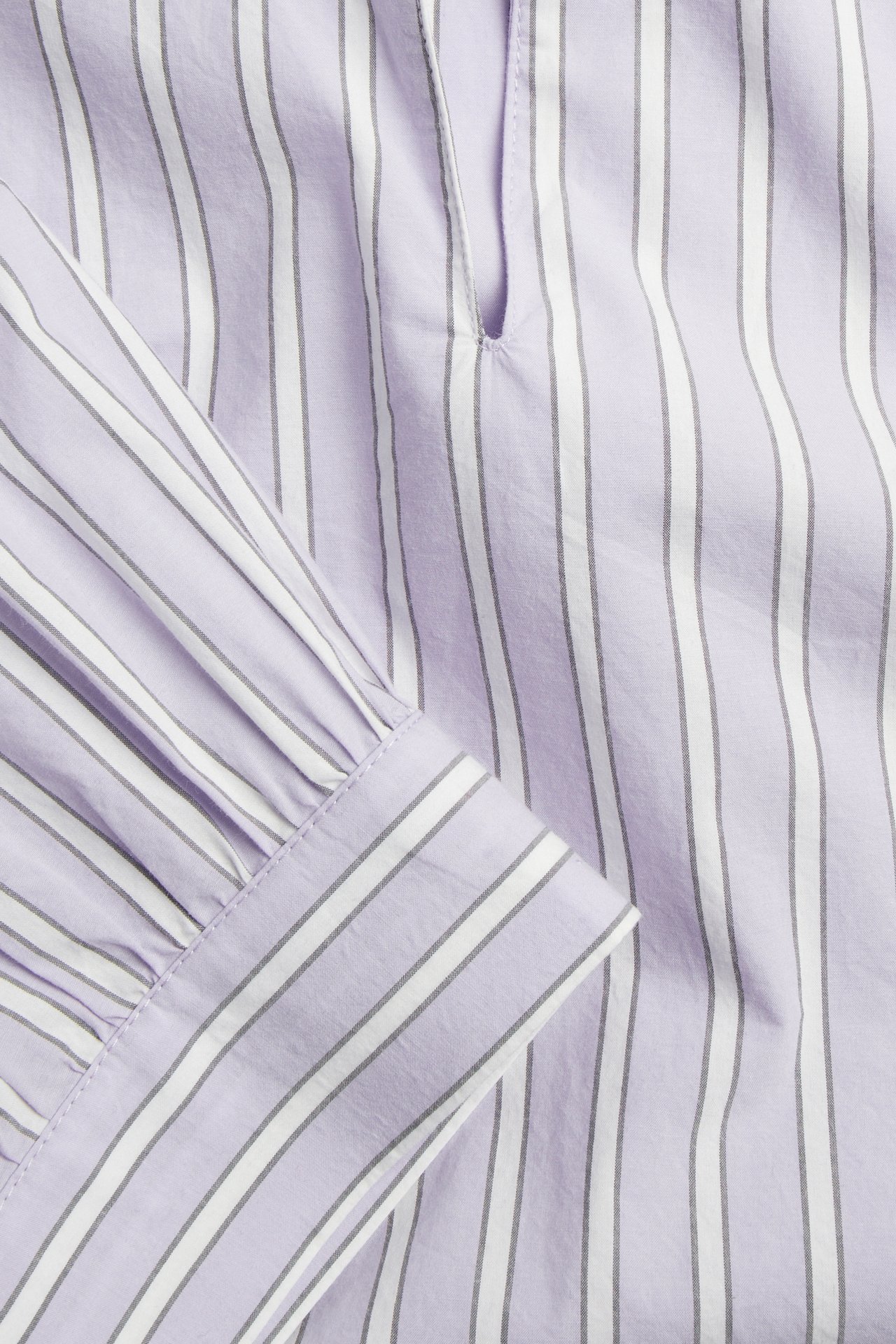 Nærbilde av en lys lilla bomullspoplinbluse med hvite og grå striper og en rynket puffermmansjett.