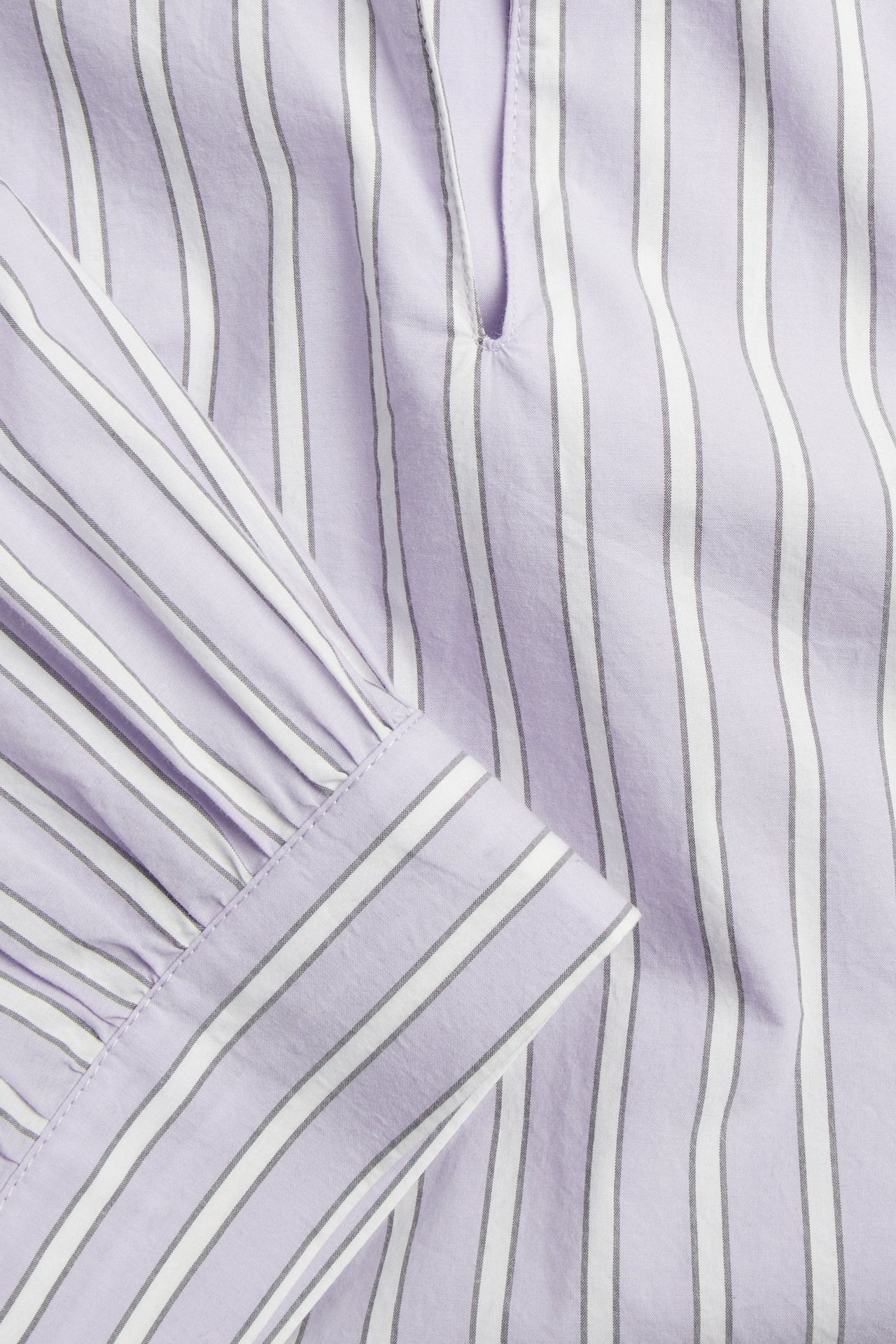 Nærbilde av en lys lilla bomullspoplinbluse med hvite og grå striper og en rynket puffermmansjett.