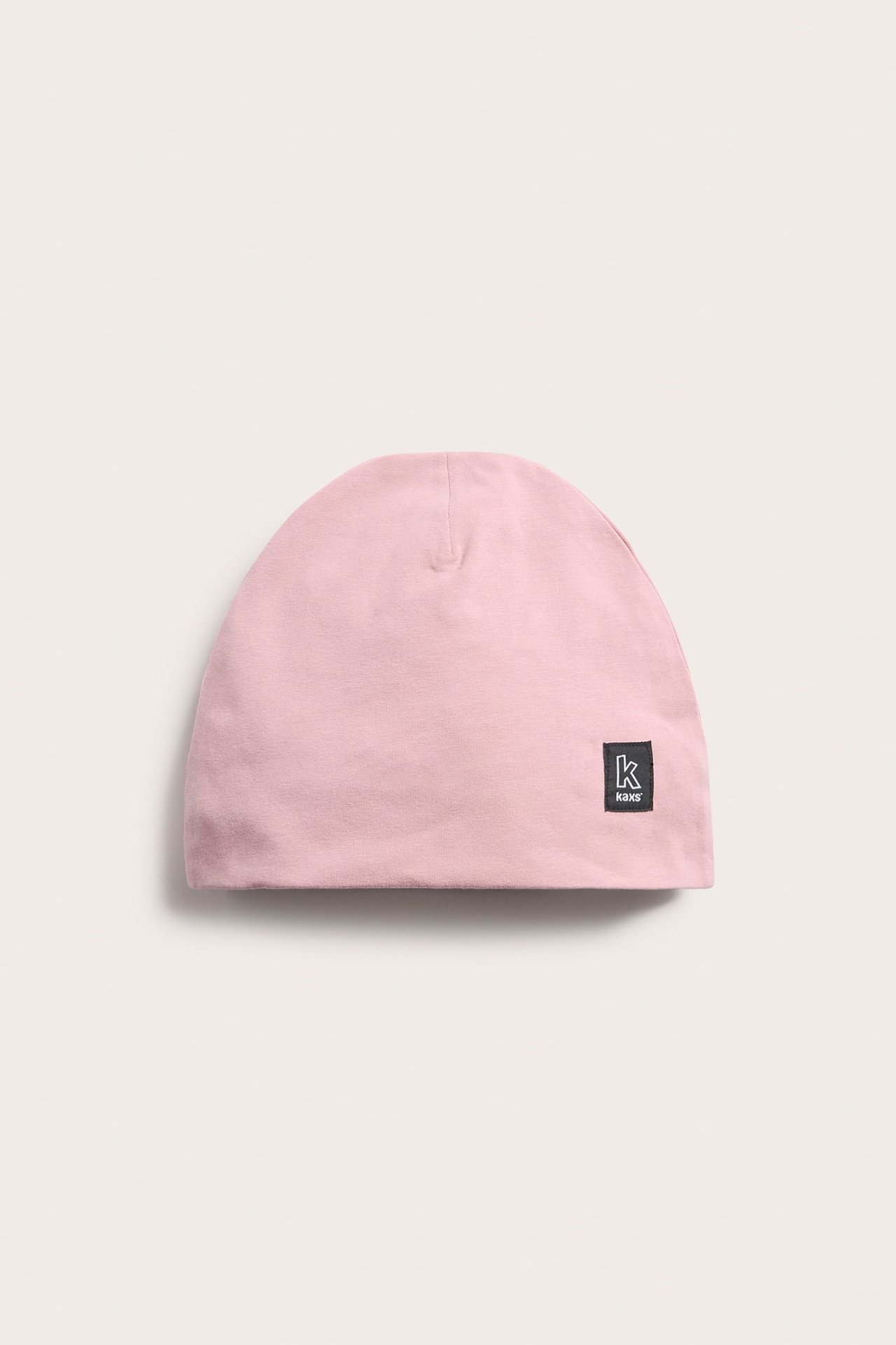 Widok z przodu jednokolorowej różowej czapki beanie z dżerseju z małą, czarną metką Kaxs.