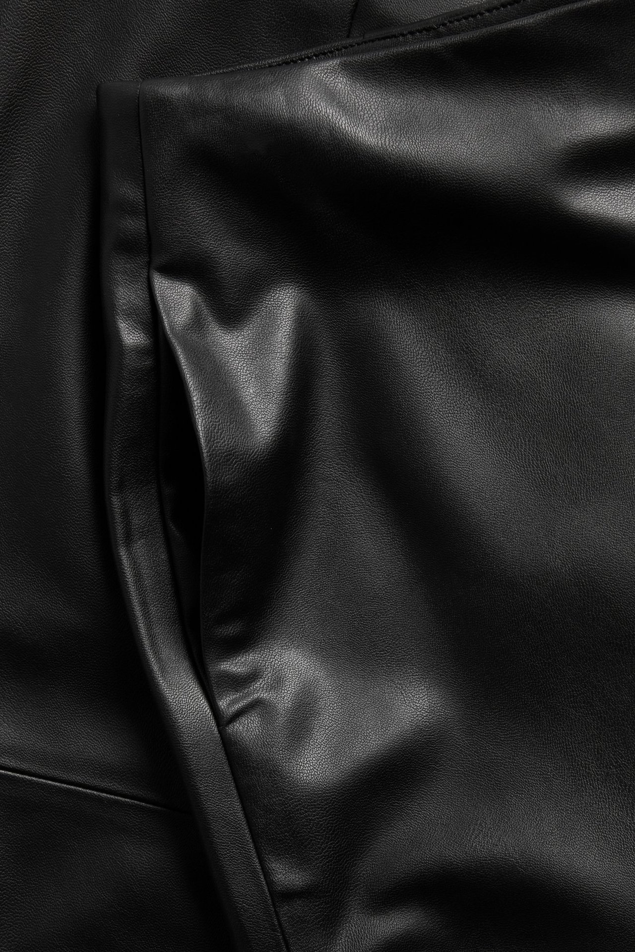 Zbliżenie na czarną ołówkową spódnicę z imitacji skóry, widać fakturę tkaniny i otwór kieszeni.