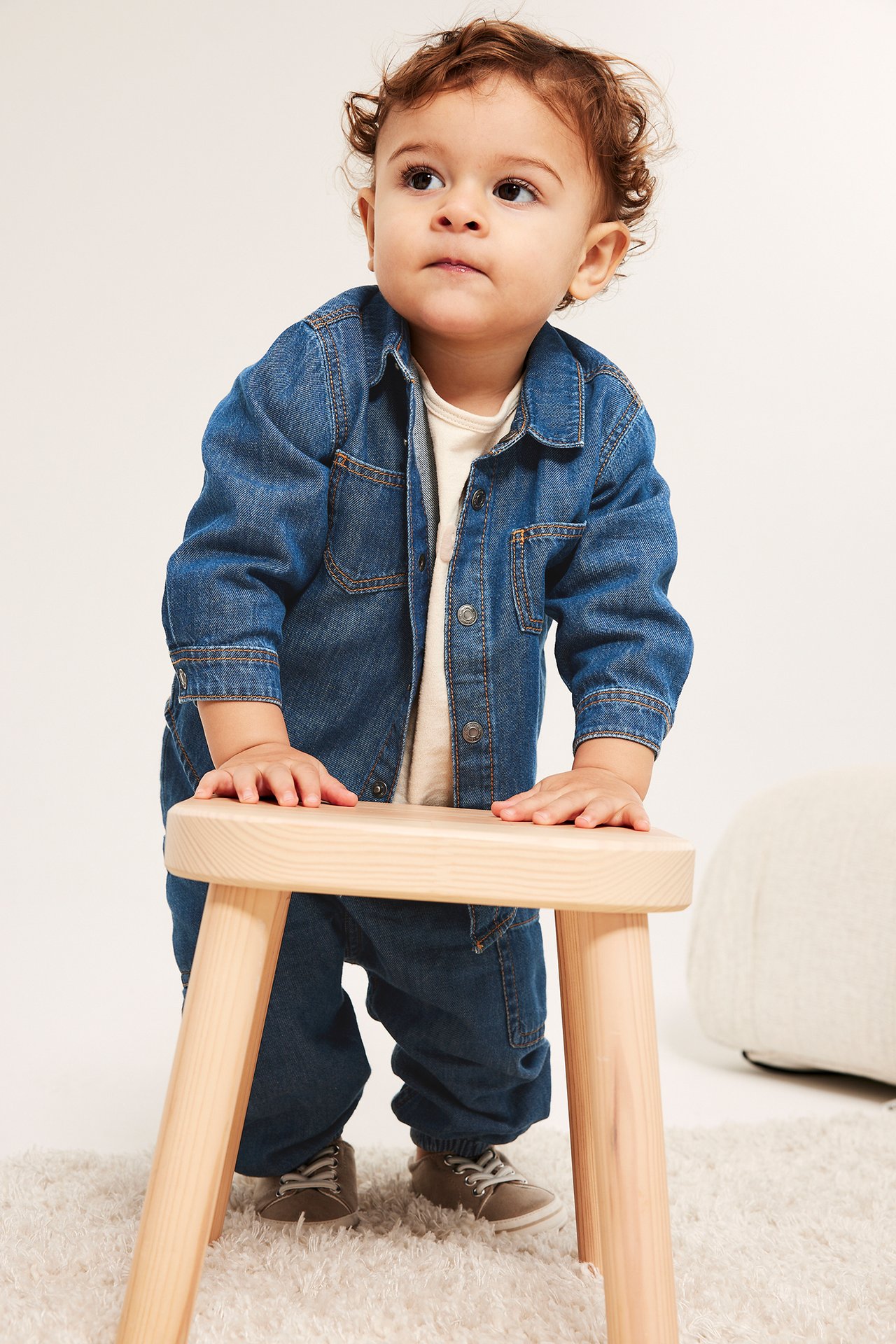 Forfra, en baby i mørk dongeriskjorte med trykknapper, matchende dongeribukse og grå sko.