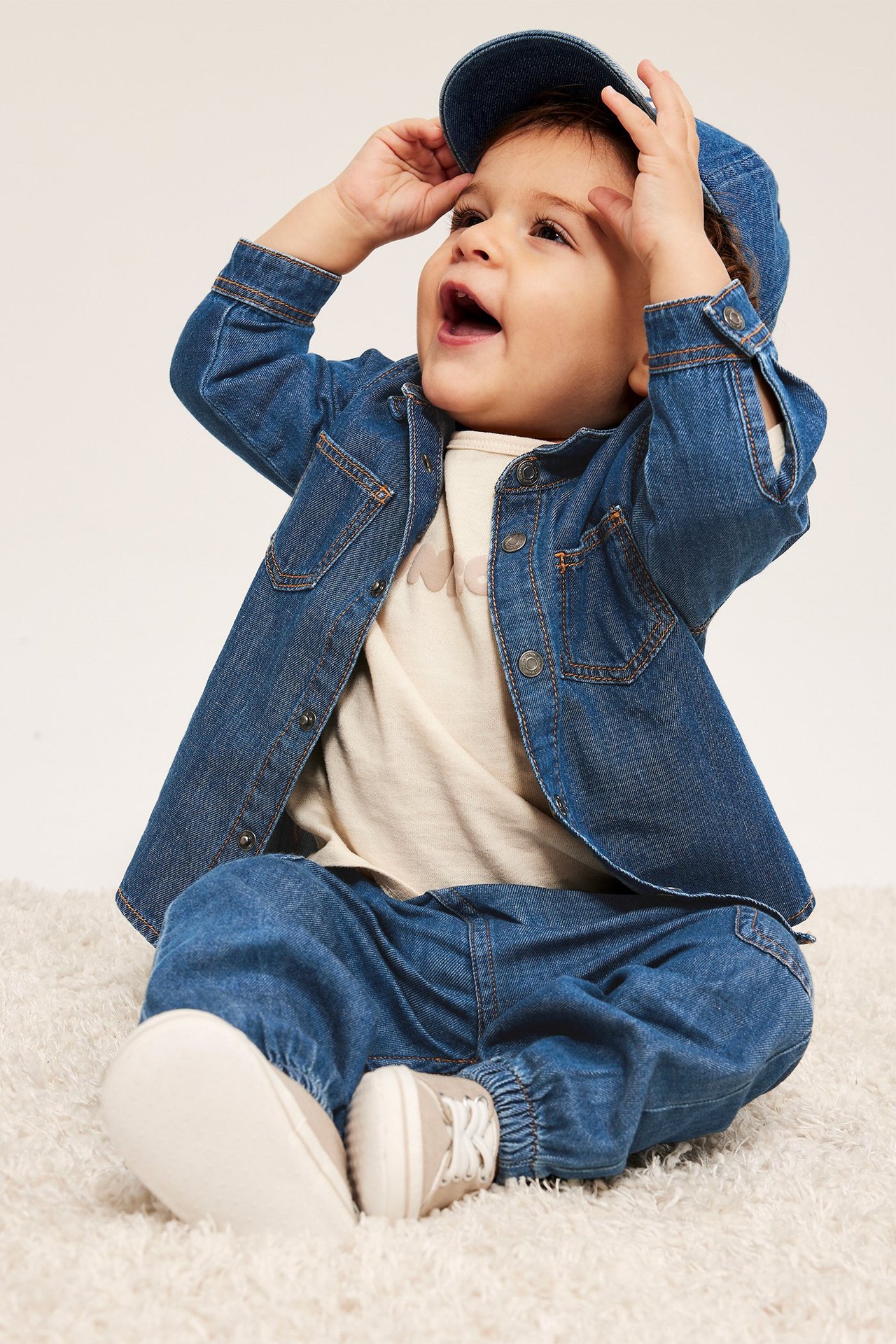 Forfra: baby i mørk denimskjorte, lys t-skjorte, mørk denim bukse, caps og lyse sko.