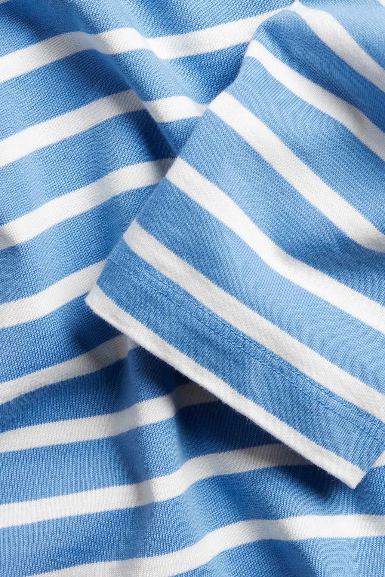 Zbliżenie na niebiesko-białą bluzkę w paski z bawełnianego dżerseju z widocznym mankietem.