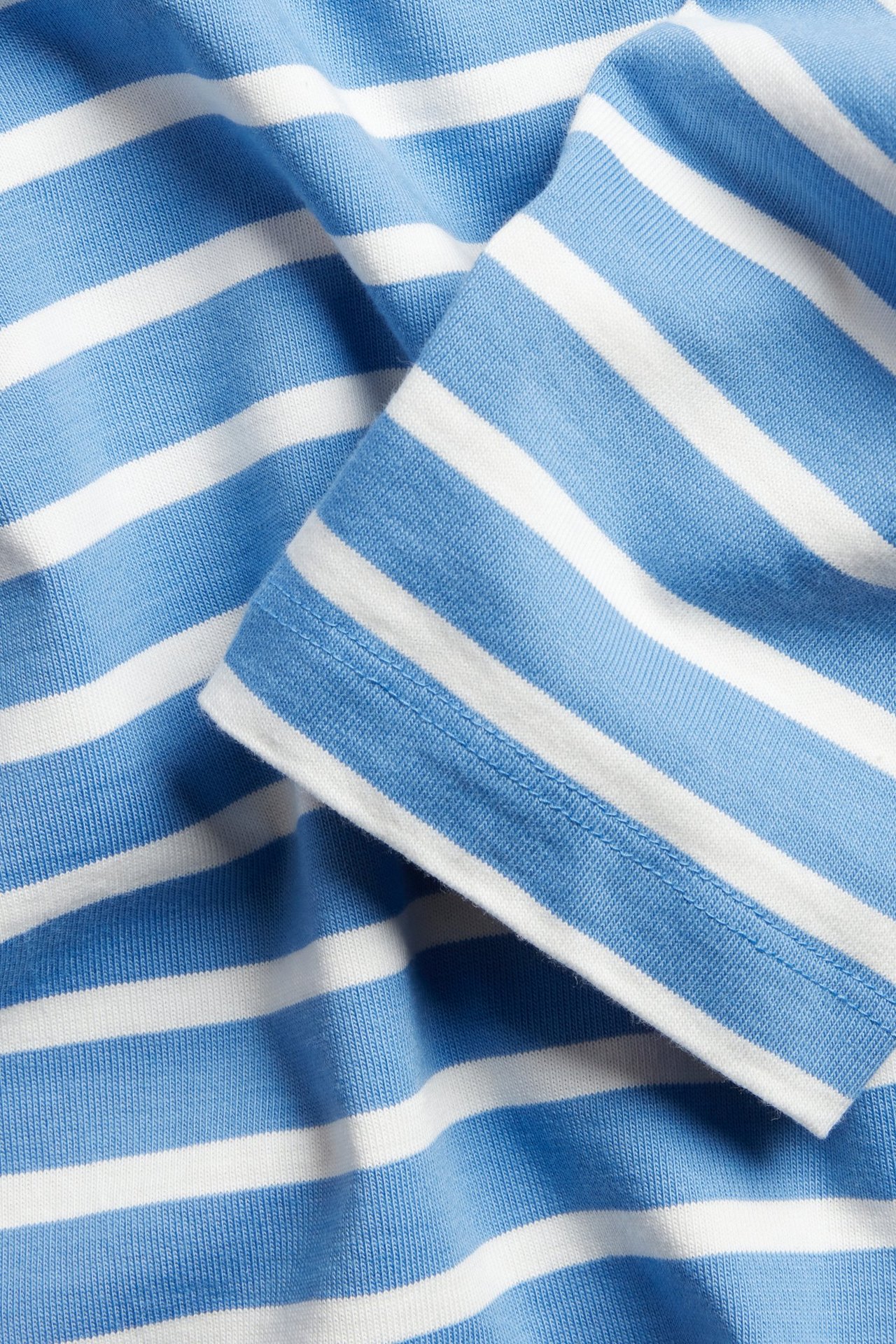 Zbliżenie na niebiesko-białą bluzkę w paski z bawełnianego dżerseju z widocznym mankietem.