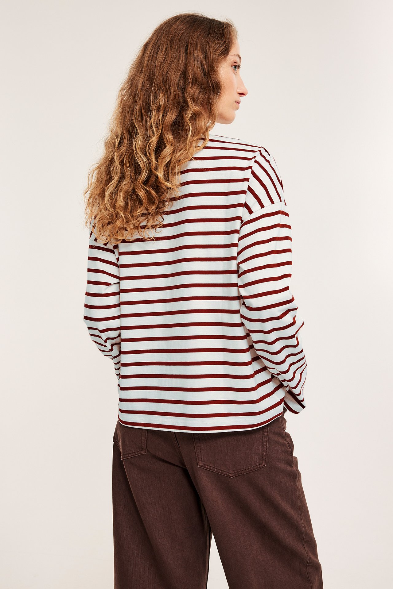 Naisen takasivu: valko-punaraitainen pitkähihainen raskas jerseypusero ja ruskeat leveälahkeiset housut.