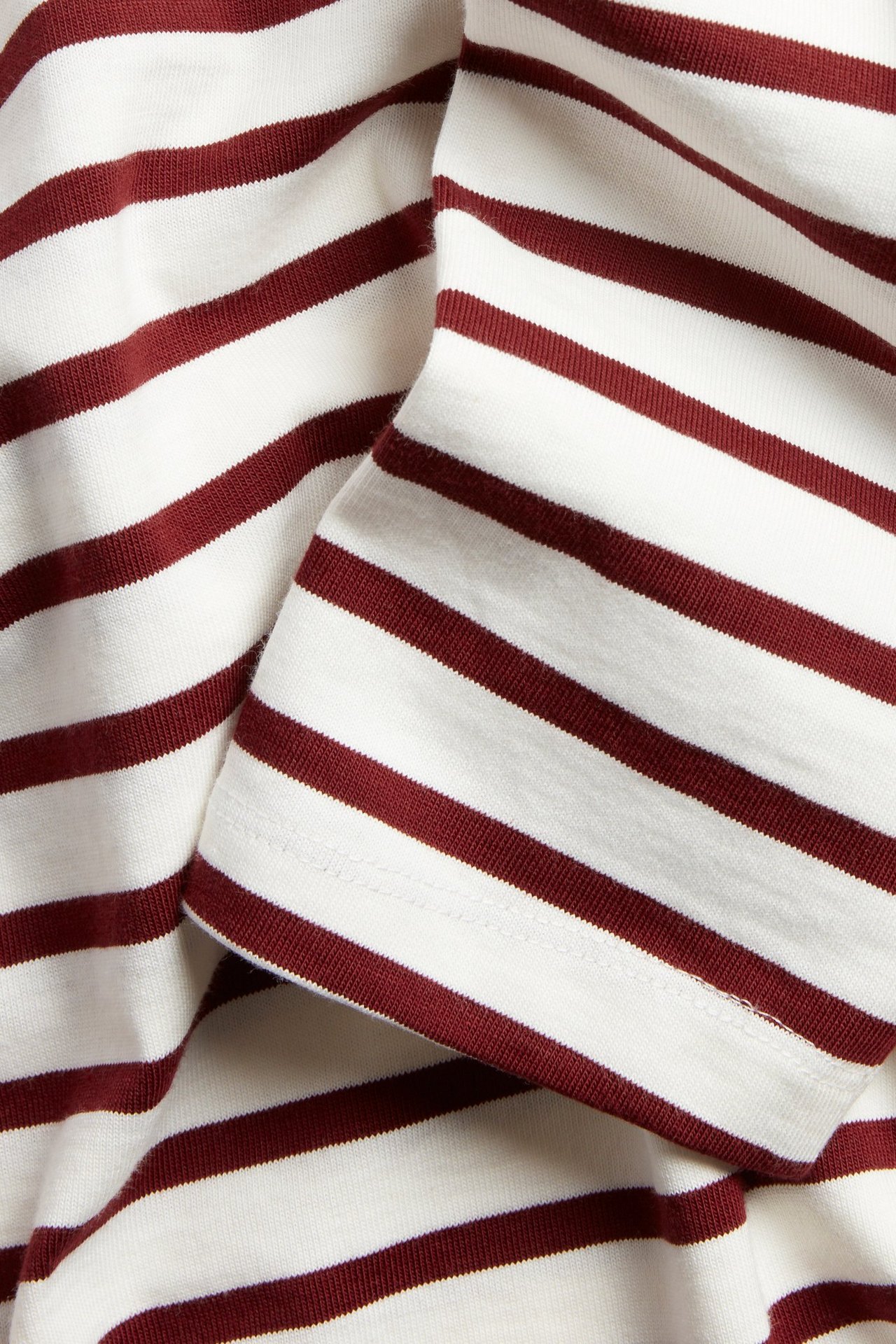 Zbliżenie białego, długiego topu z grubej dzianiny w czerwone paski, z widocznym mankietem.