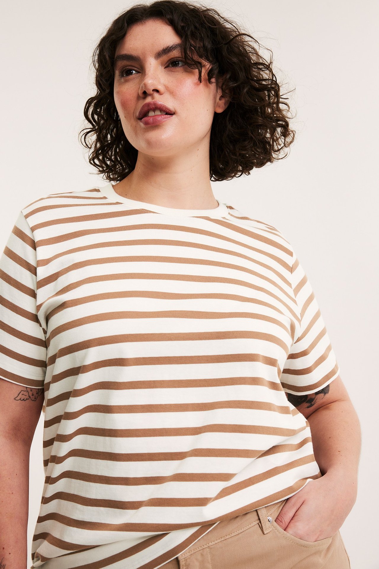 Edestäpäin, nainen yllään beige-valkoraidallinen puuvillainen lyhythihainen t-paita ja beiget housut.
