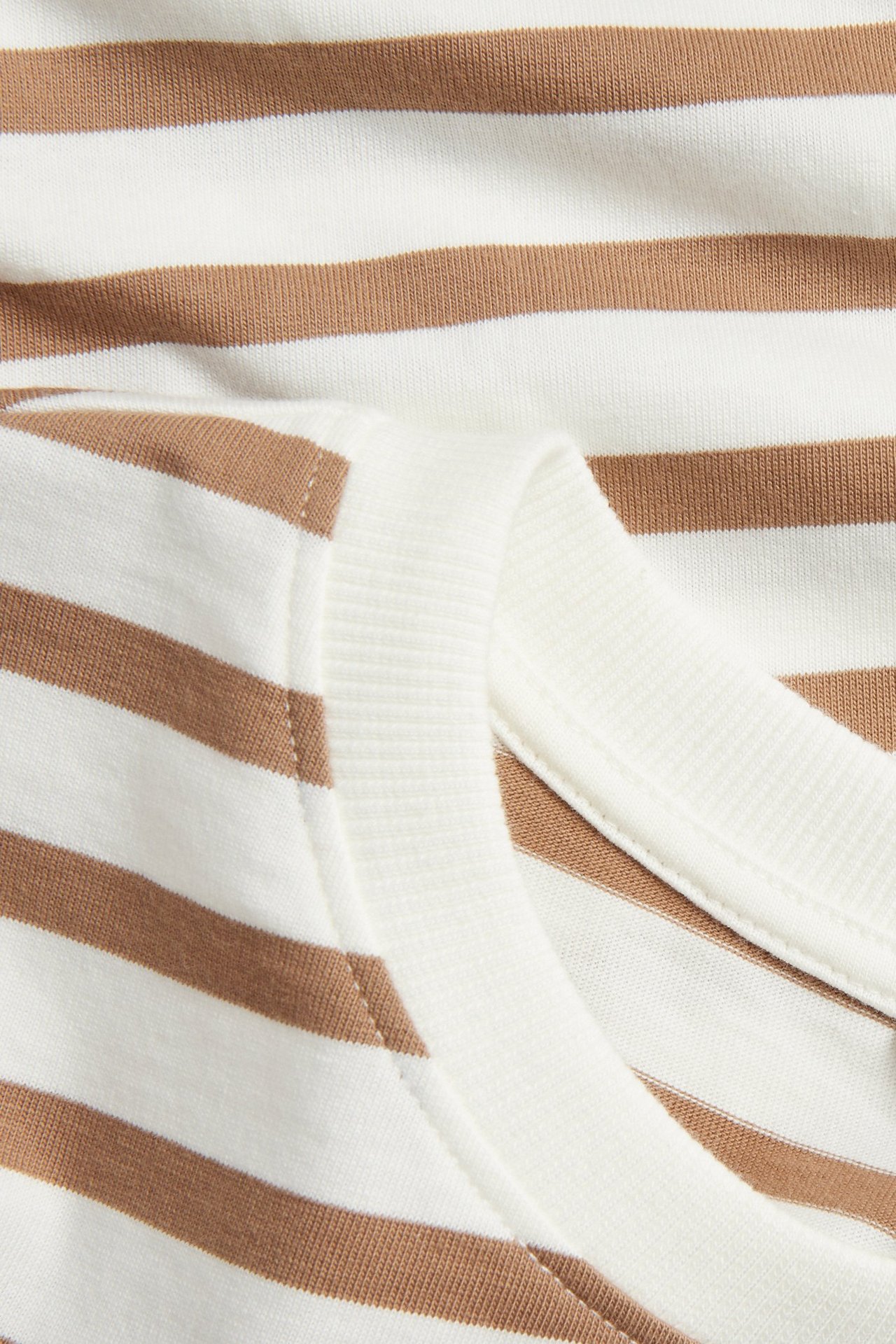 Lähikuva beigen ja valkoisen raidallisen lyhythihaisen puuvillapaidan uurretusta pääntiestä.