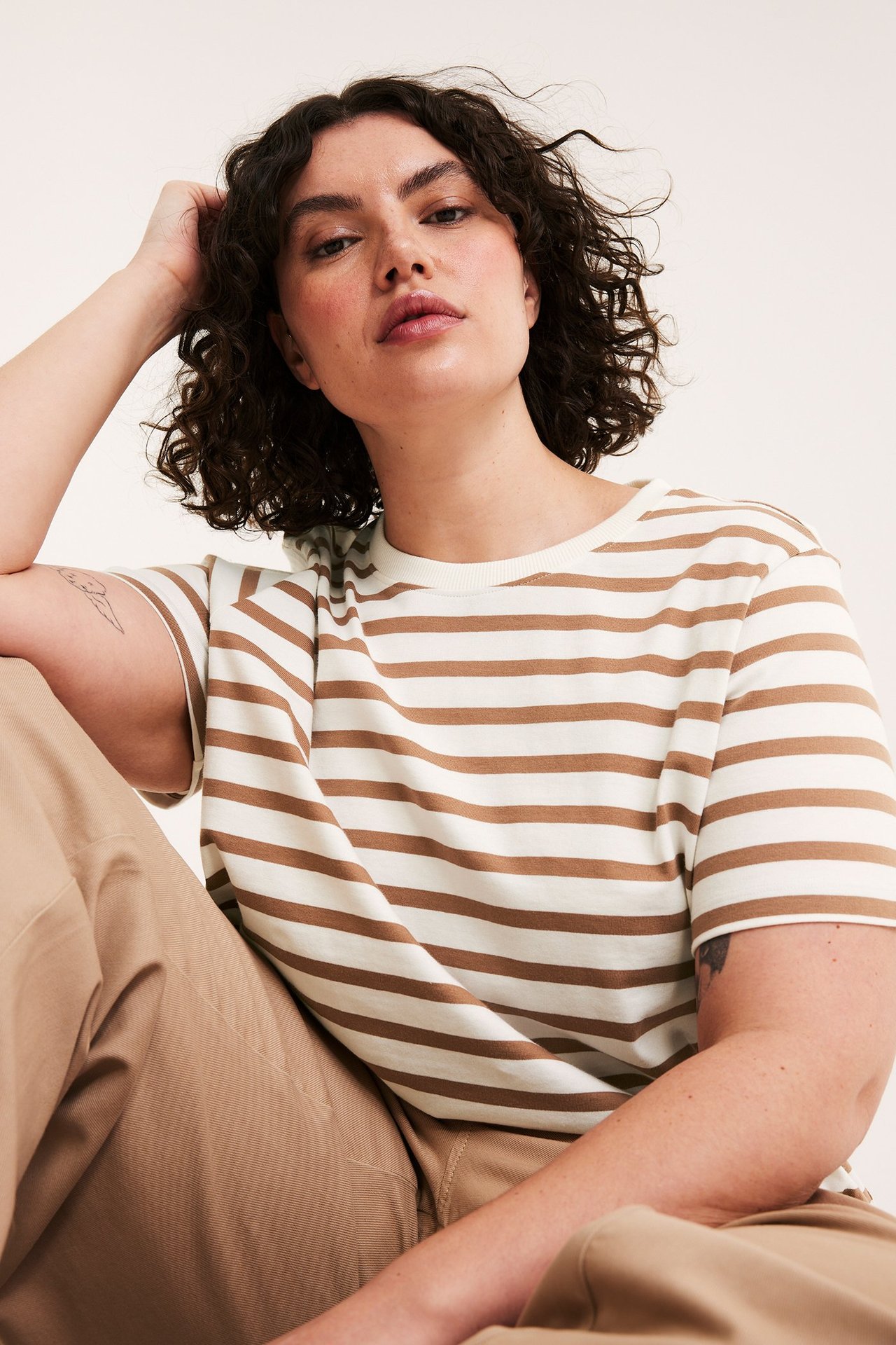 Etunäkymä, lähikuva naisesta beige-valkoraidallisessa puuvillapaidassa beigenväristen housujen kanssa.
