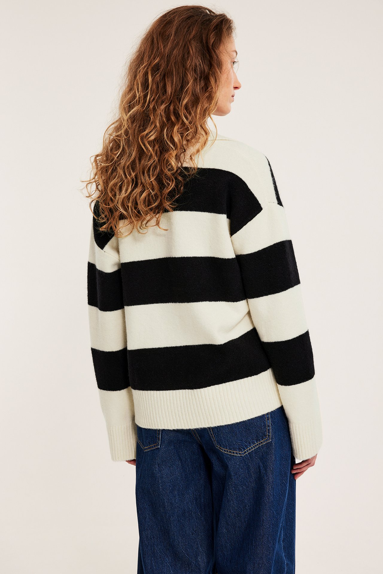 Bakfra: kvinne i myk offwhite- og svartstripet strikkegenser og blå jeans.