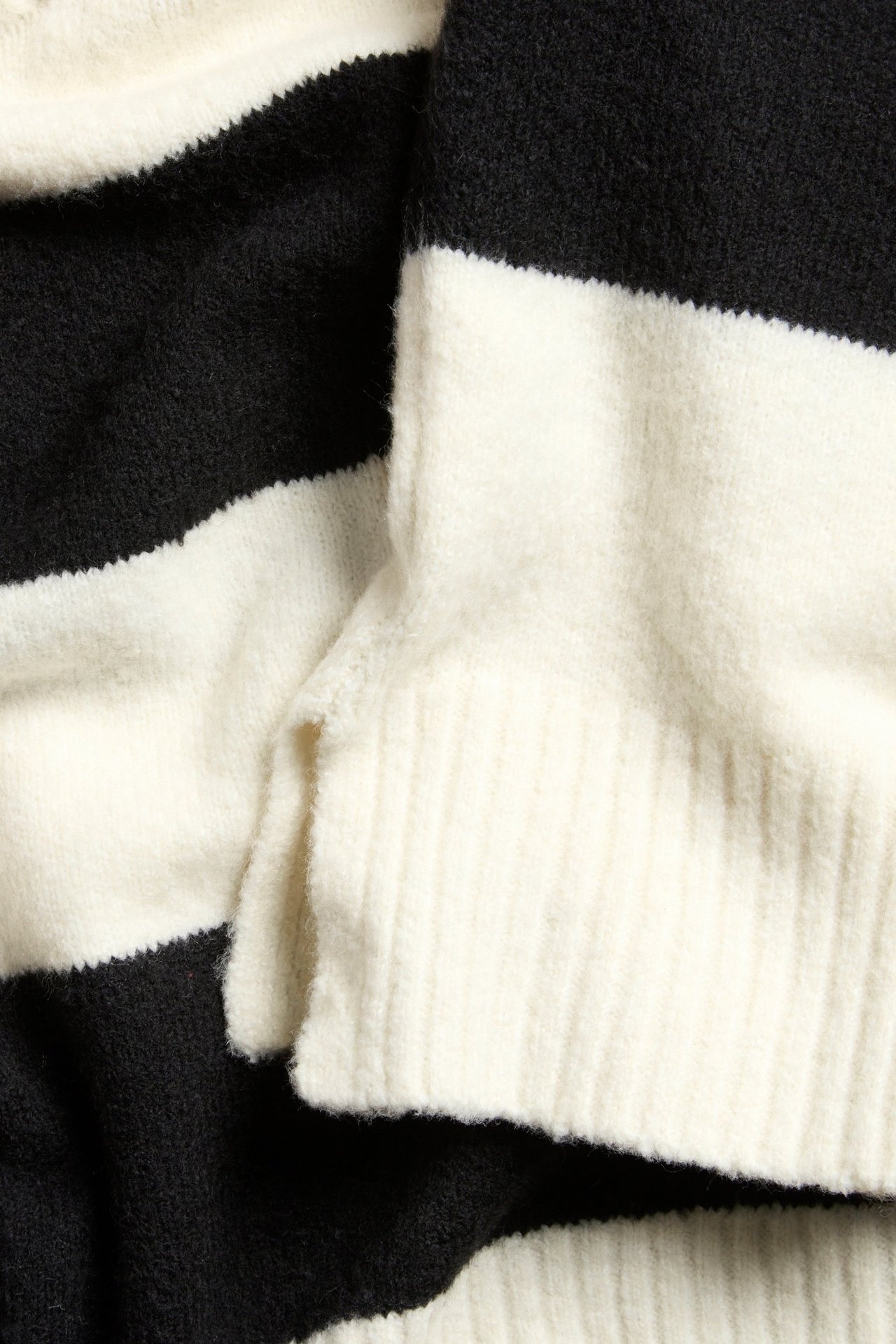 Zbliżenie na off-white i czarny dzianinowy sweter w paski z prążkowanym brzegiem.