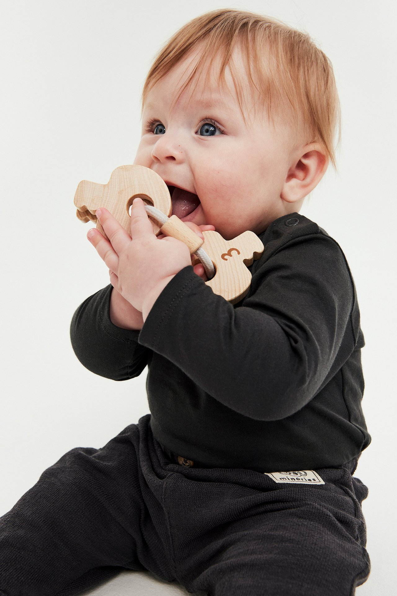 Sidebilde av en baby i en svart langermet body med skulderknapper, holder en tre-bitering.