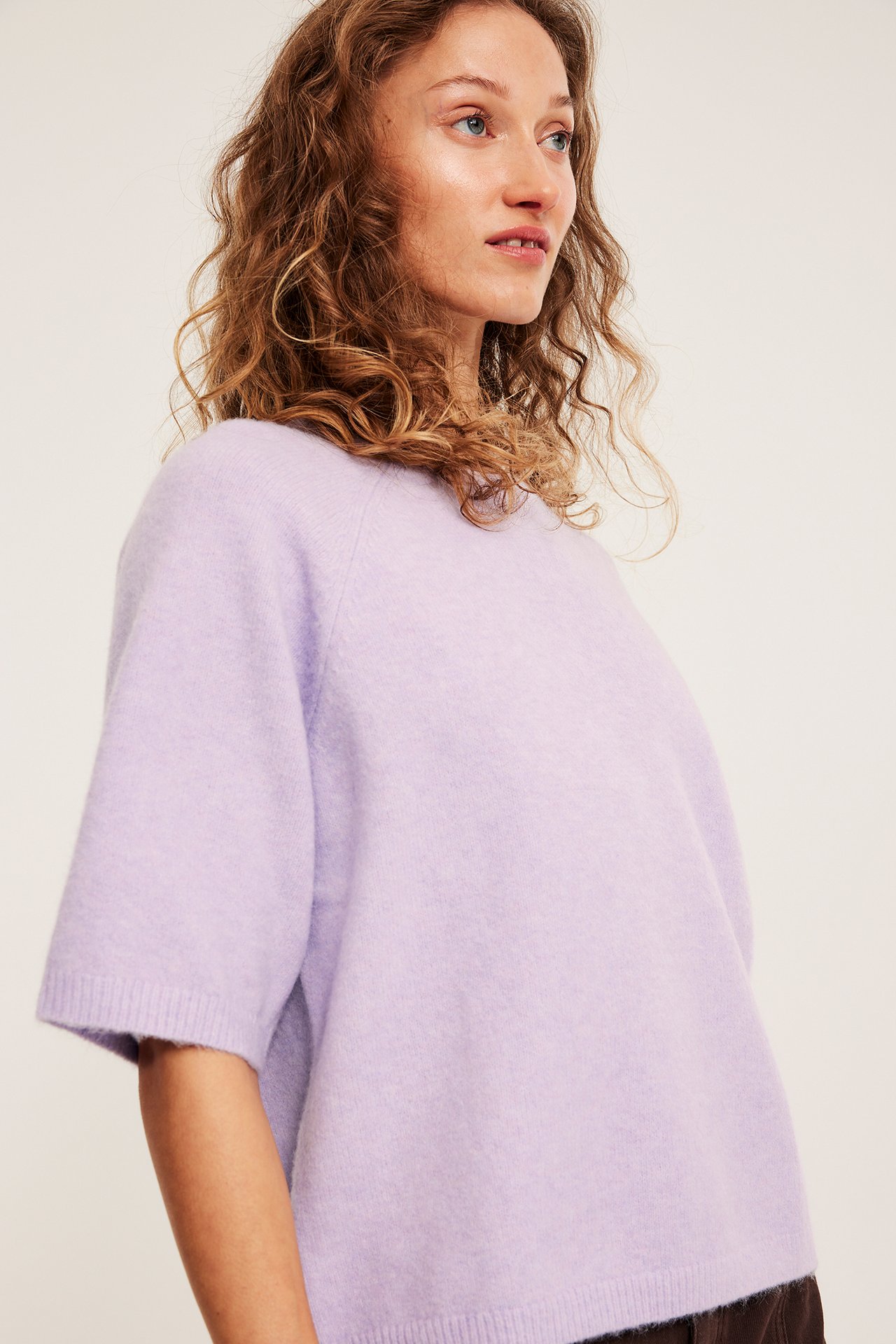 Nærbilde av en kvinne i en oversized lys lilla strikket kortermet topp.