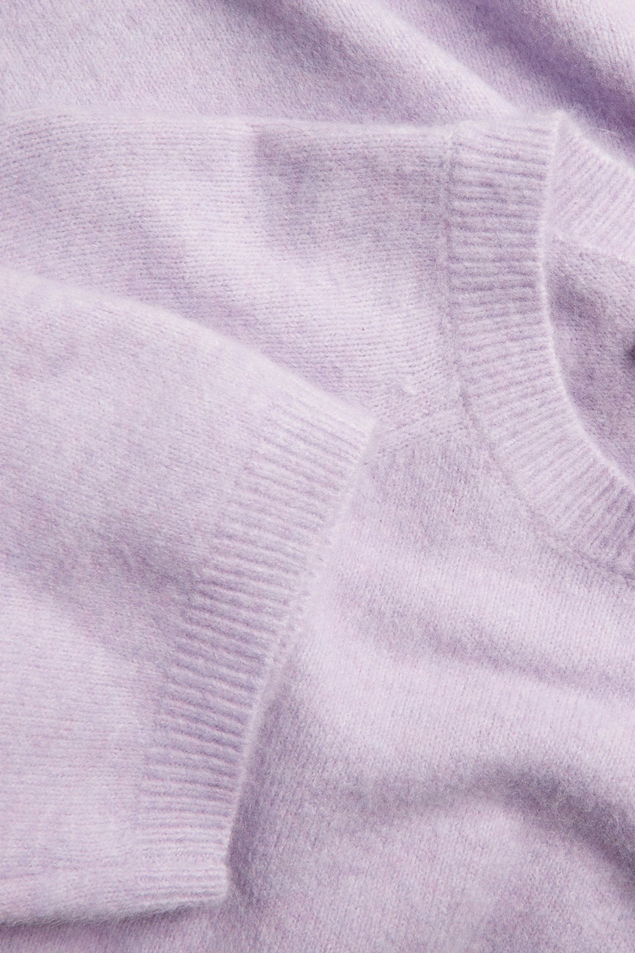 Zbliżenie: Jasnofioletowy, oversize'owy dzianinowy sweter T-shirt z prążkowanymi mankietami i dekoltem.