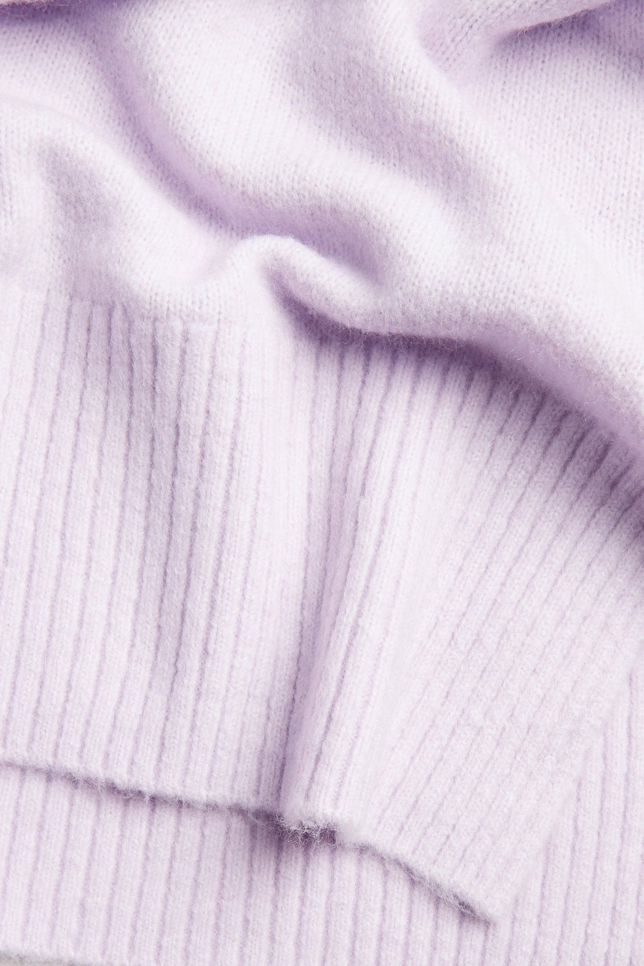 Zbliżenie na jasnofioletowy, jednolity dzianinowy sweter z miękką teksturą i prążkowanymi detalami.
