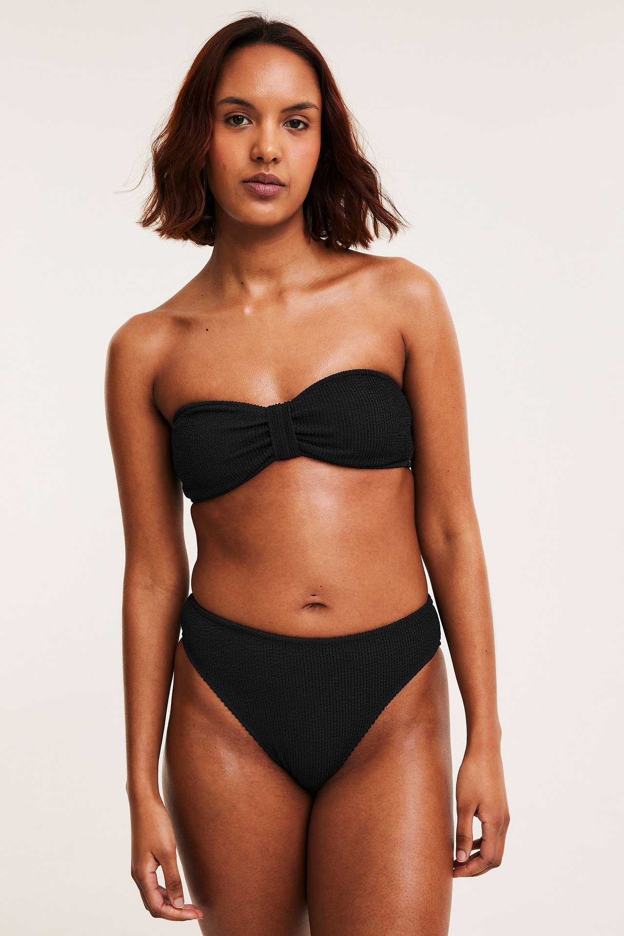 Edestäpäin, nainen yllään musta kuvioitu korkeavyötäröinen brazilian-bikinihousu ja yhteensopiva olkaimeton yläosa.