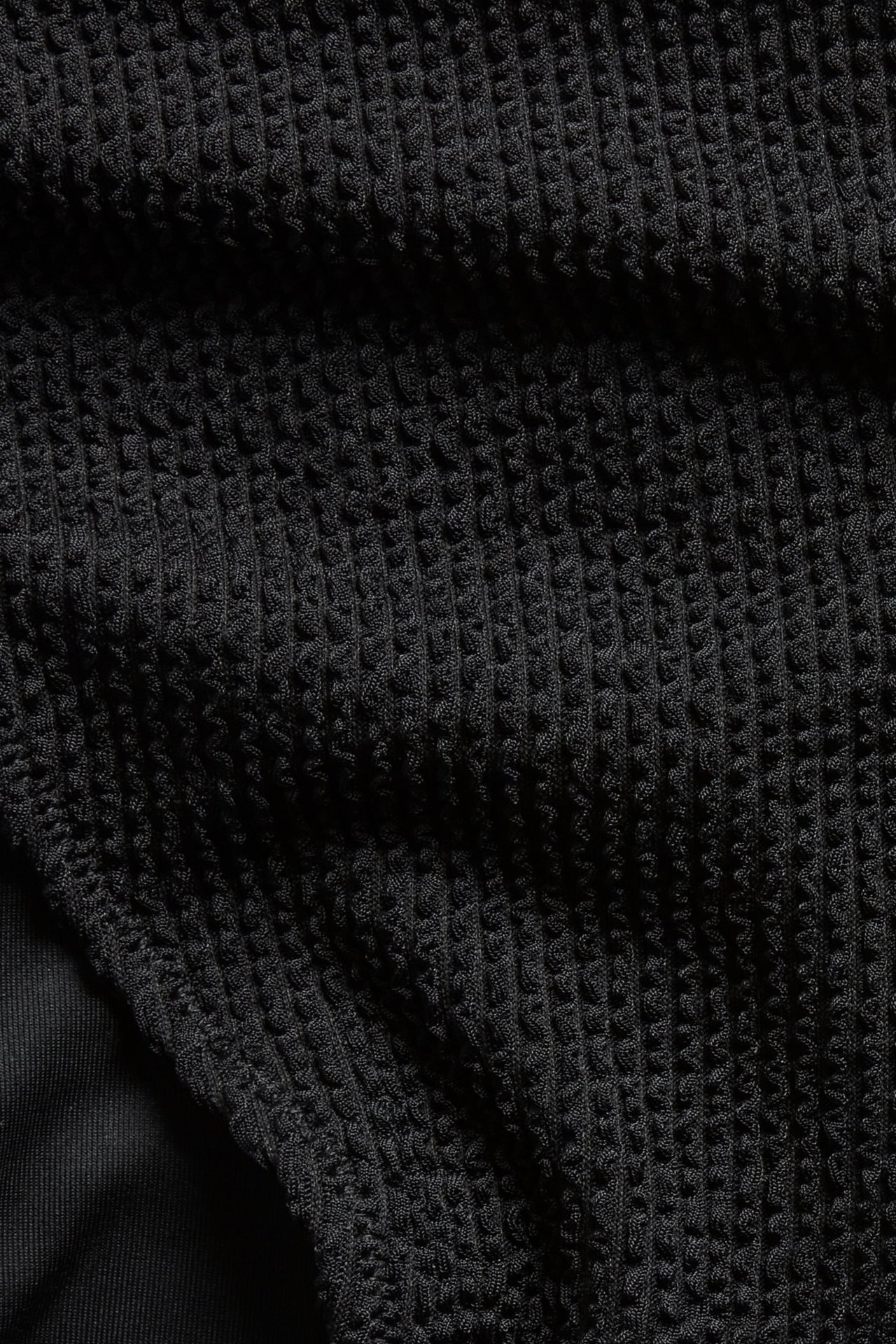 Zbliżenie na czarny, fakturowany materiał od dołu bikini.