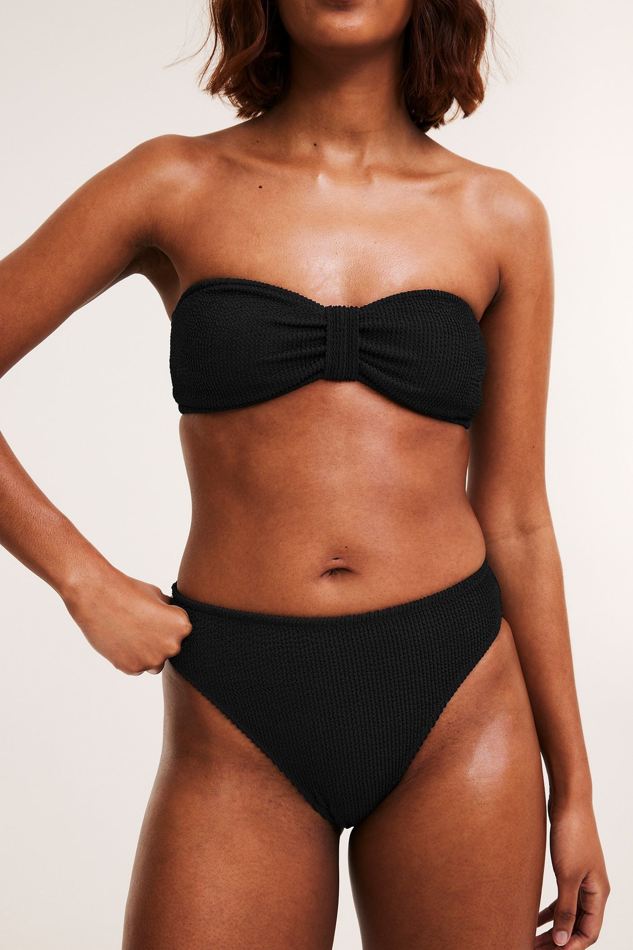 Nainen edestä, yllään musta strukturoitu korkeavyötäröinen brazilian-bikinihousu ja yhteensopiva yläosa.