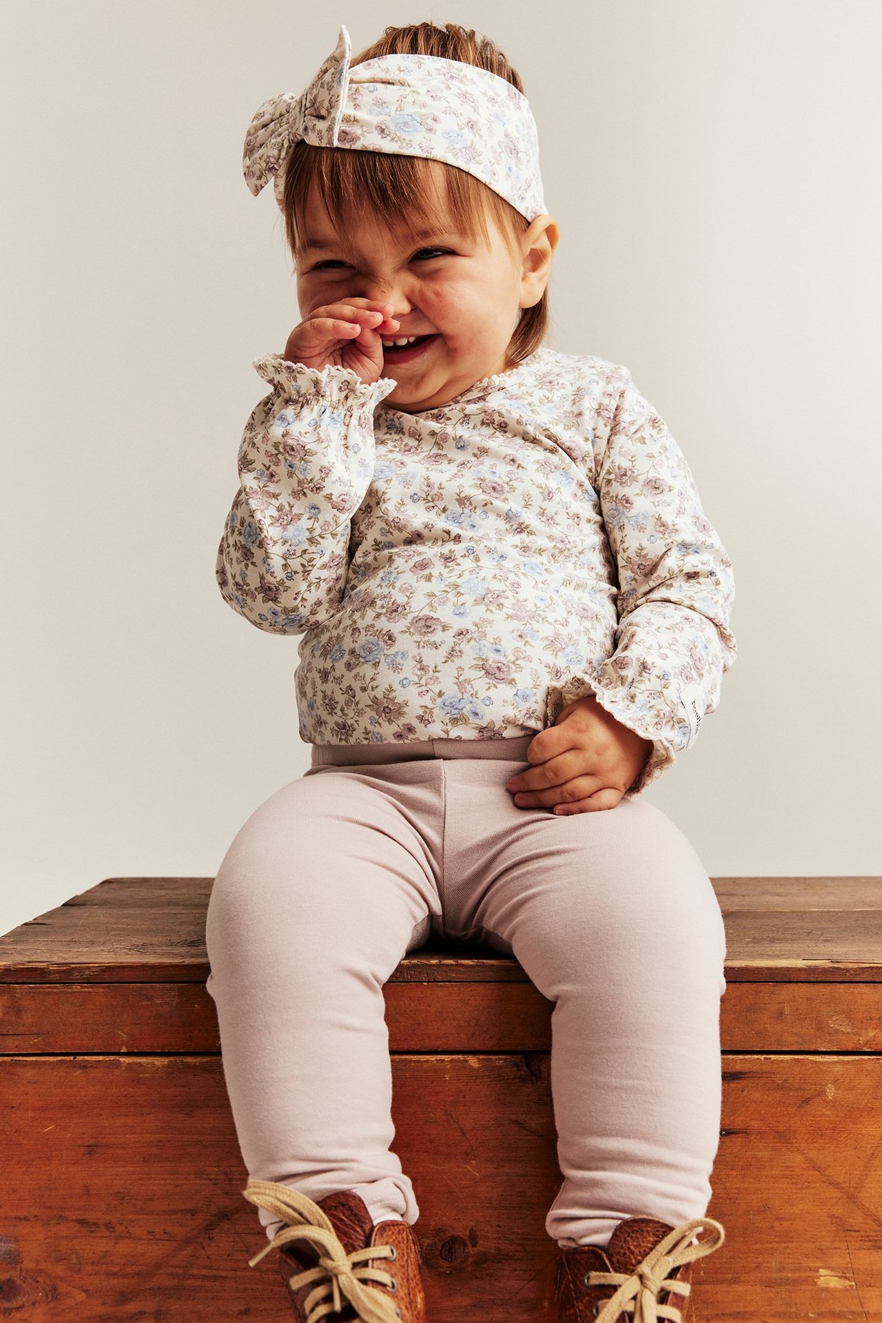 Frontvisning av baby i offwhite blomstret langermet body, rosa leggings og matchende blomstret pannebånd.