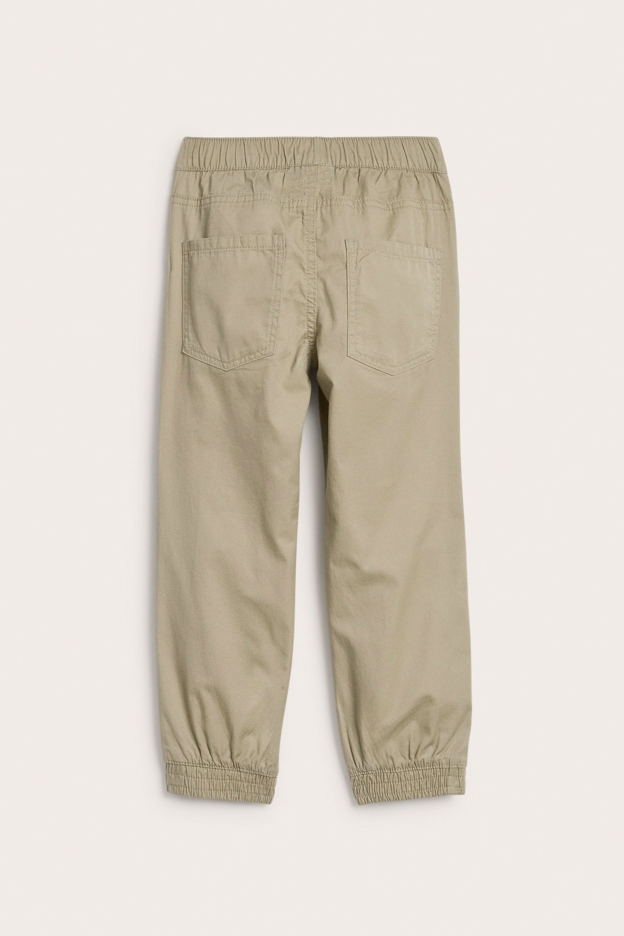 Bakifrån av barnbyxor i beige vävd bomull med resår i midja och benslut, med två bakfickor.