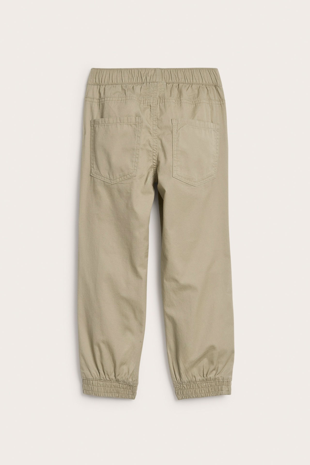Bakifrån av barnbyxor i beige vävd bomull med resår i midja och benslut, med två bakfickor.