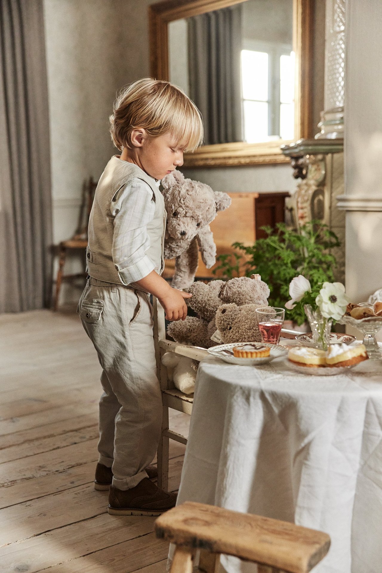 Sidovy av ett barn i beiga vävda byxor, en ljusbeige väst och en ljusrutig skjorta.