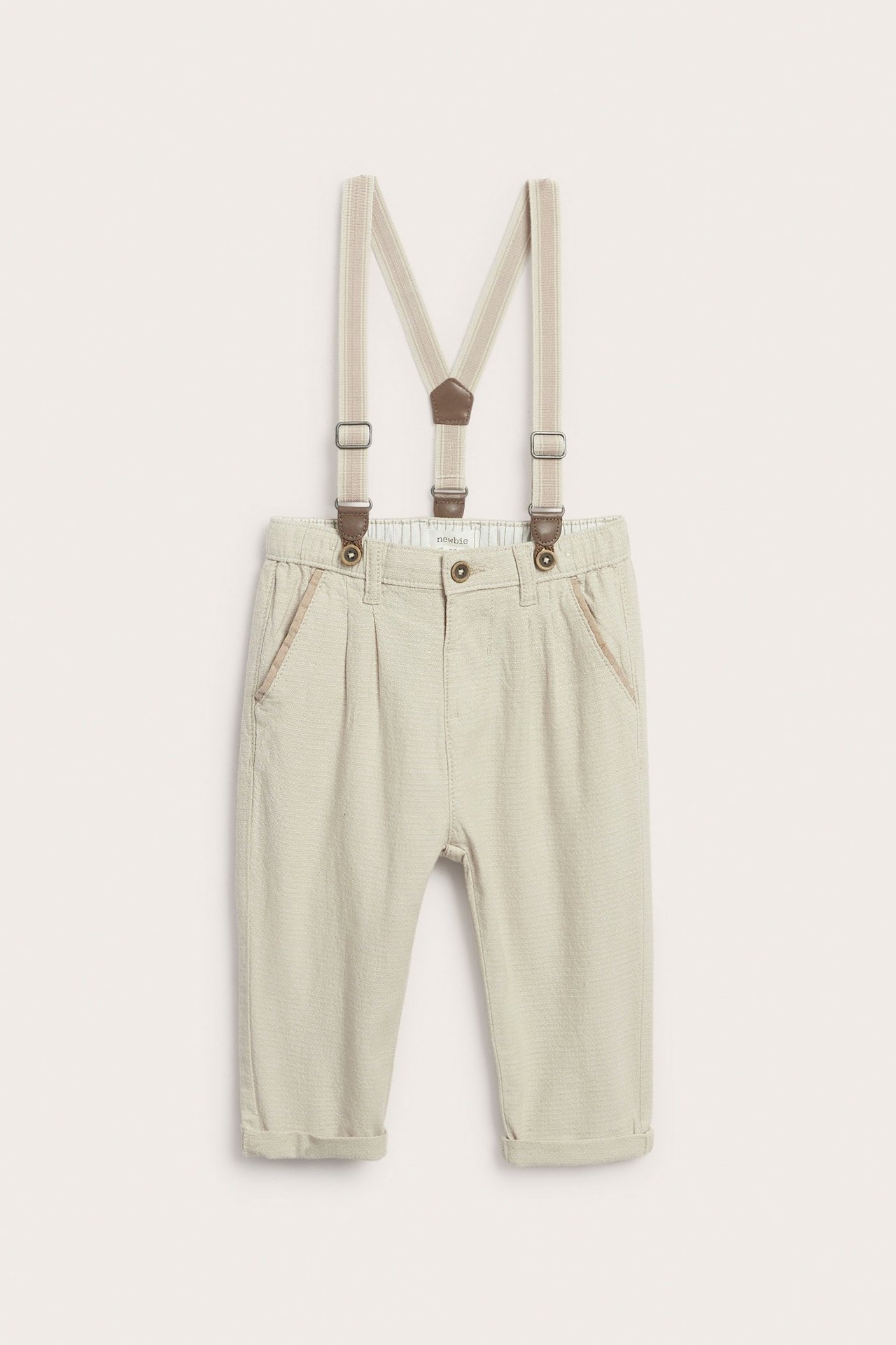 Edestä: Beiget kudotut lasten housut, säädettävät beiget henkselit ja rullatut lahkeensuut.