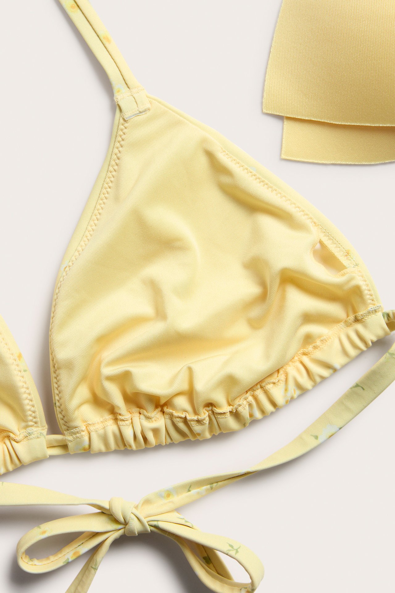 Nærbilde av en gul blomstret trekant-bikinitopp med knyting og to avtagbare innlegg.