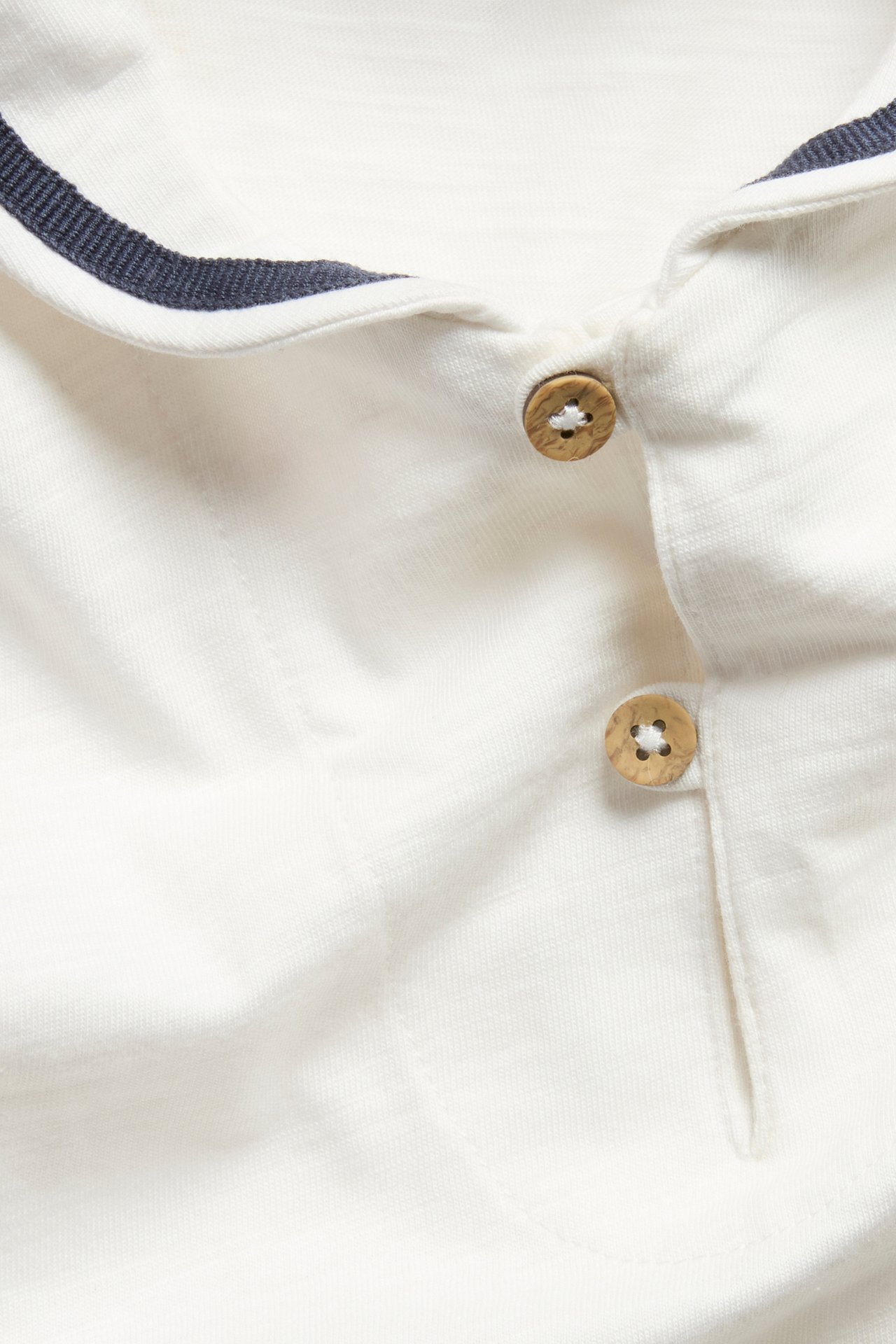 Lähikuva luonnonvalkoisesta vauvan body-paidasta, jossa on laivastonsininen merimieskaulus ja puunapit.