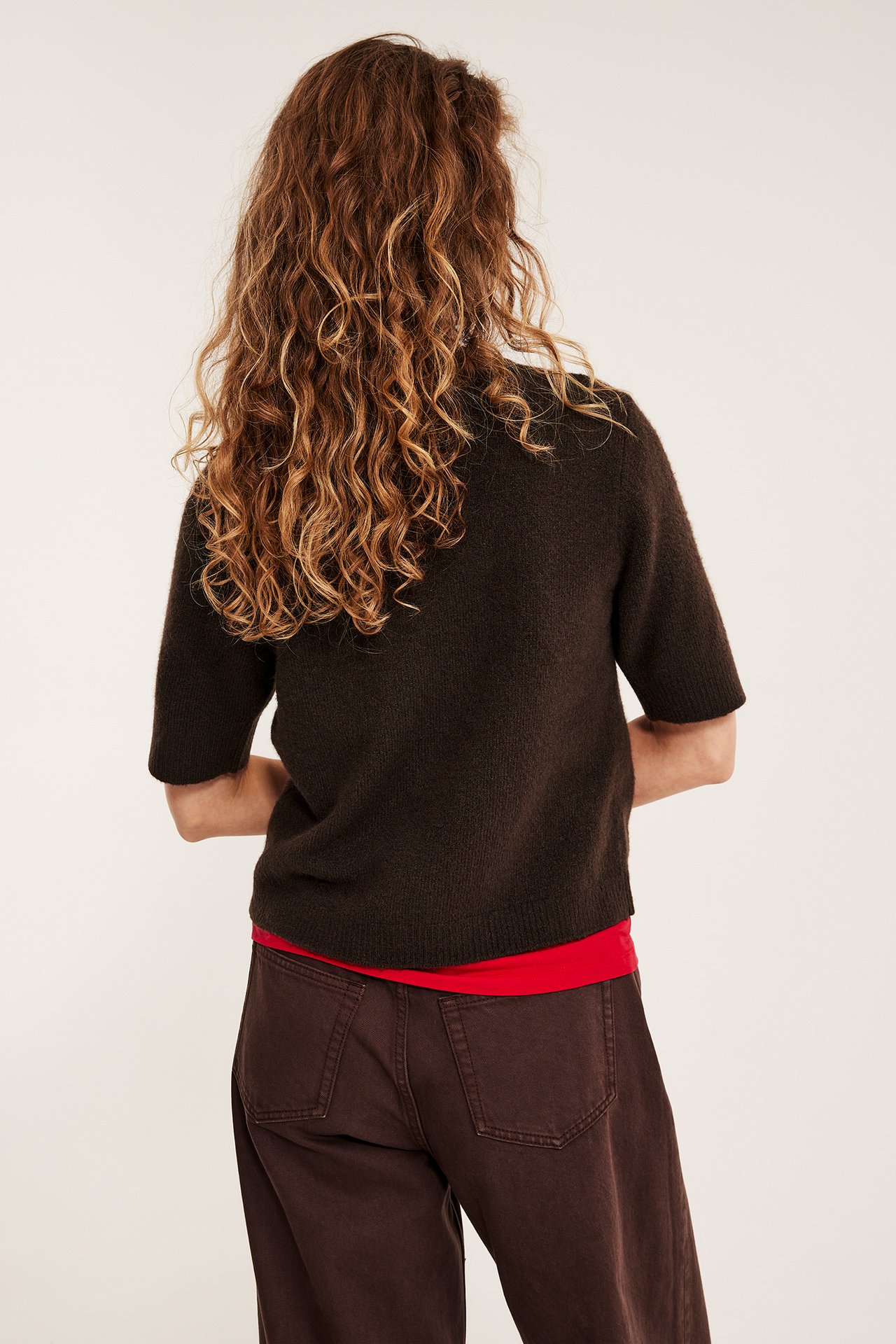 Takakuva: nainen yllään tummanruskea lyhythihainen neuletoppi, punainen toppi ja tummanruskeat housut.