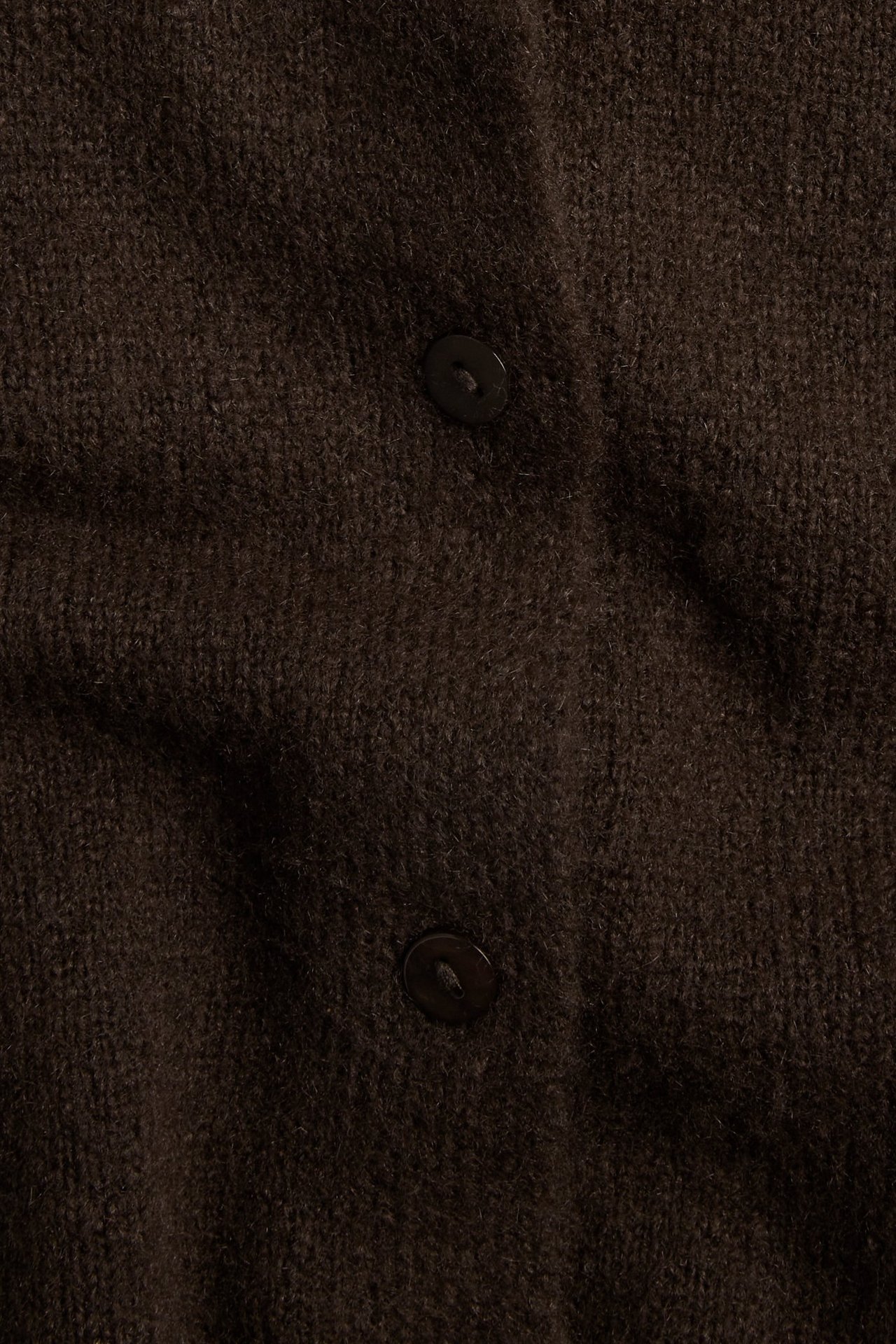 Zbliżenie na ciemnobrązowy, dzianinowy, krótkoręki sweter rozpinany z dwoma widocznymi guzikami.