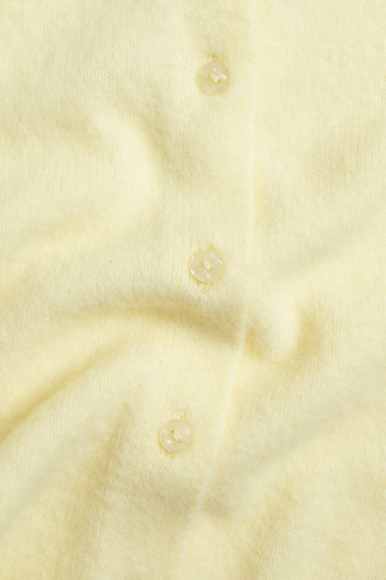 Zbliżenie na jasnożółty, dzianinowy, krótki kardigan z trzema widocznymi przezroczystymi guzikami z przodu.