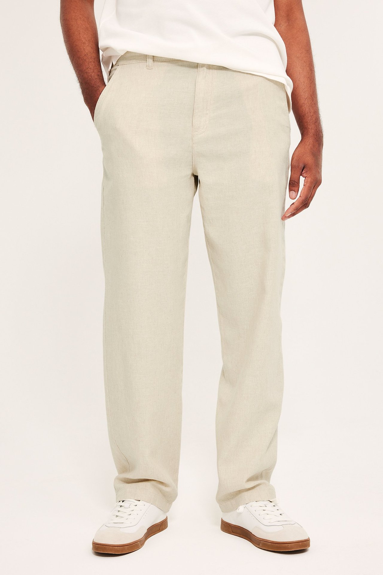 Edestä mies yllään beiget pellavasekoite housut, valkoinen t-paita ja valko-beiget tennarit.