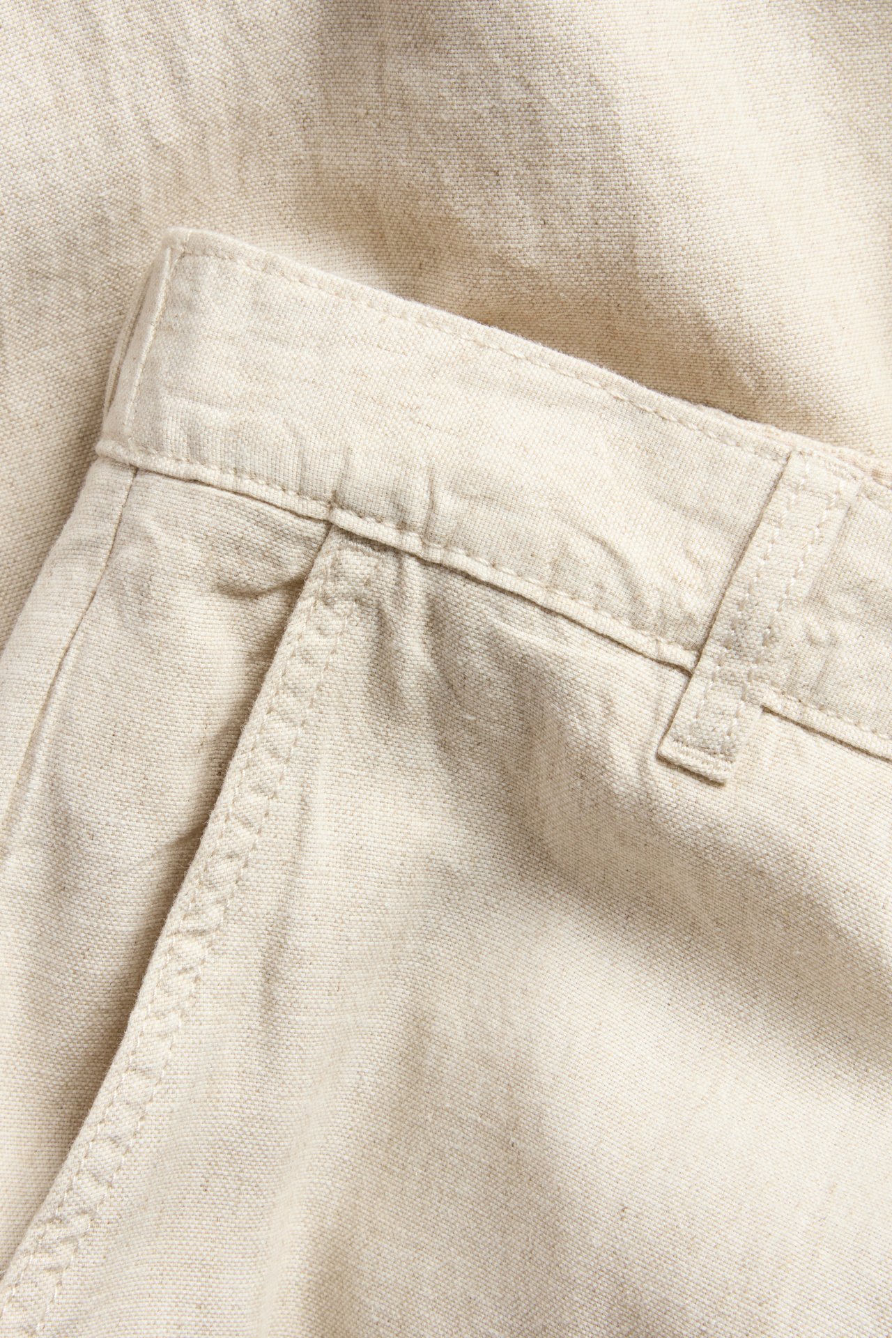 Lähikuva beigestä regular fit pellavasekoitehousuista, näyttäen vyötärönauhan, vyölenkin ja taskun suun.
