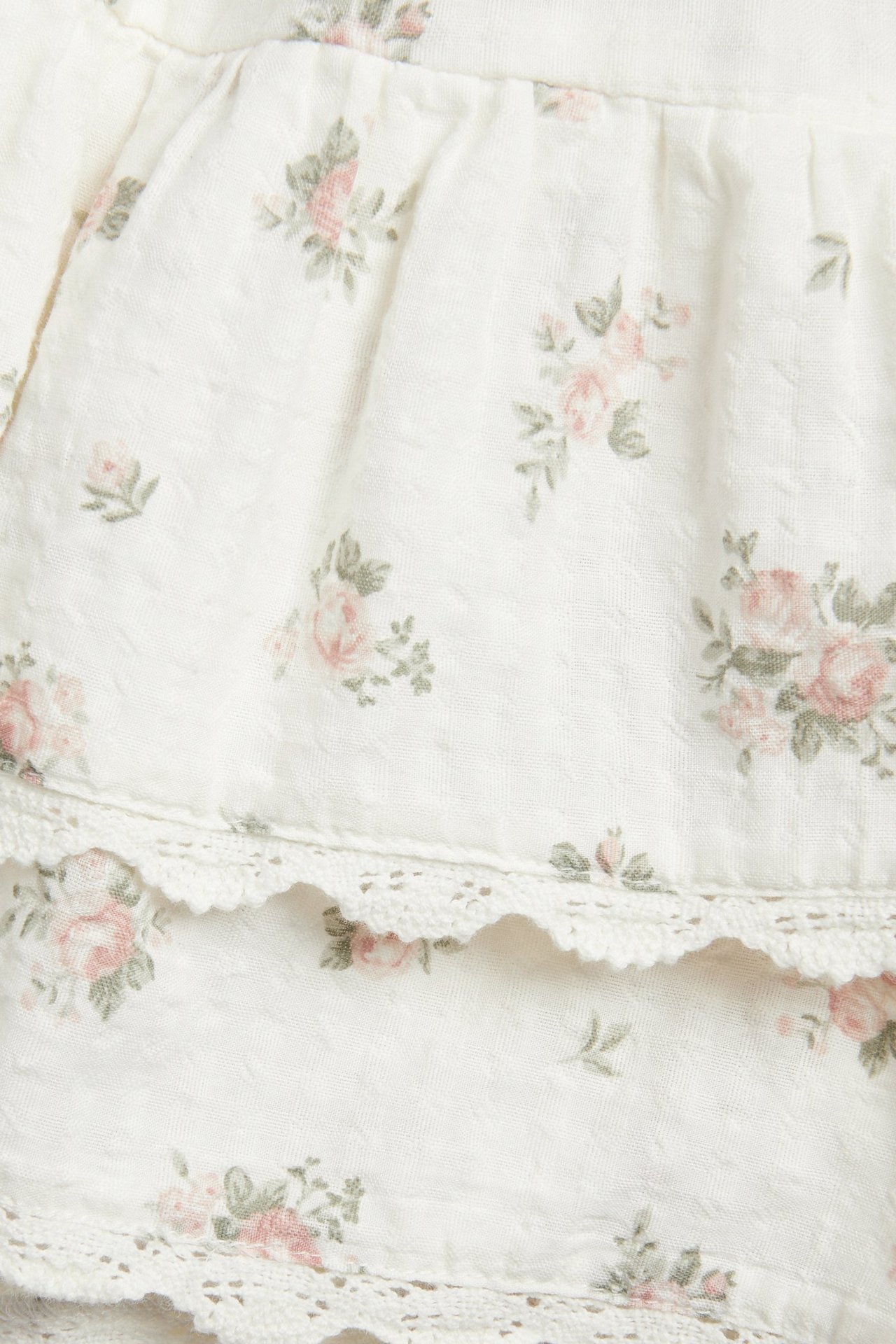 Nærbilde av et offwhite bomulls-shorts-skjørt med rosa blomstermønster og blondekantede volanger.