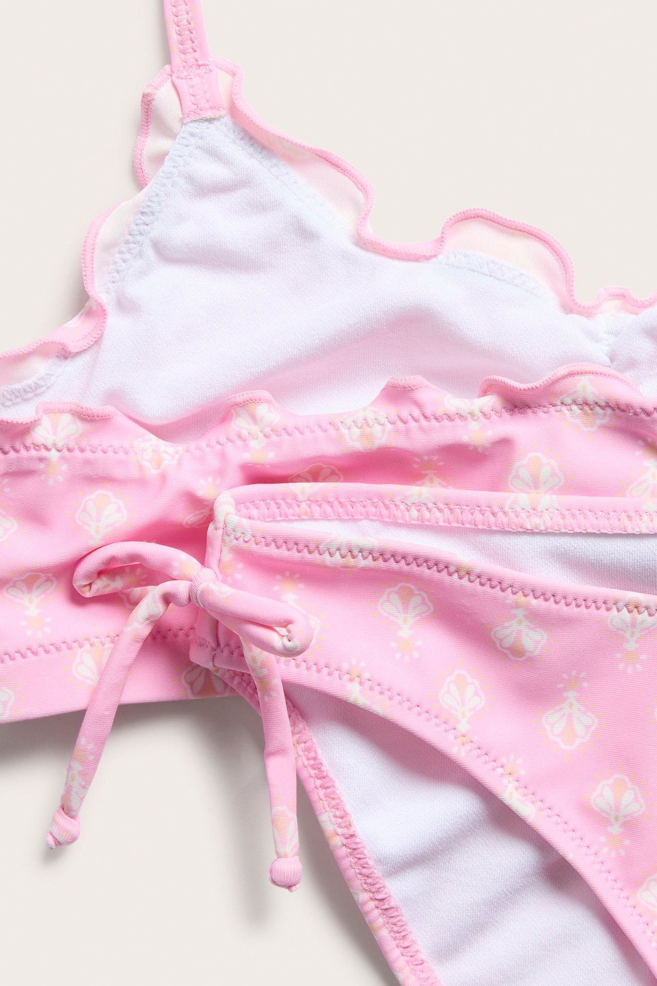 Lähikuva lapsen kuvioidusta vaaleanpunaisesta bikinipaidasta röyhelöillä ja alaosasta sivusidontanyöreillä.