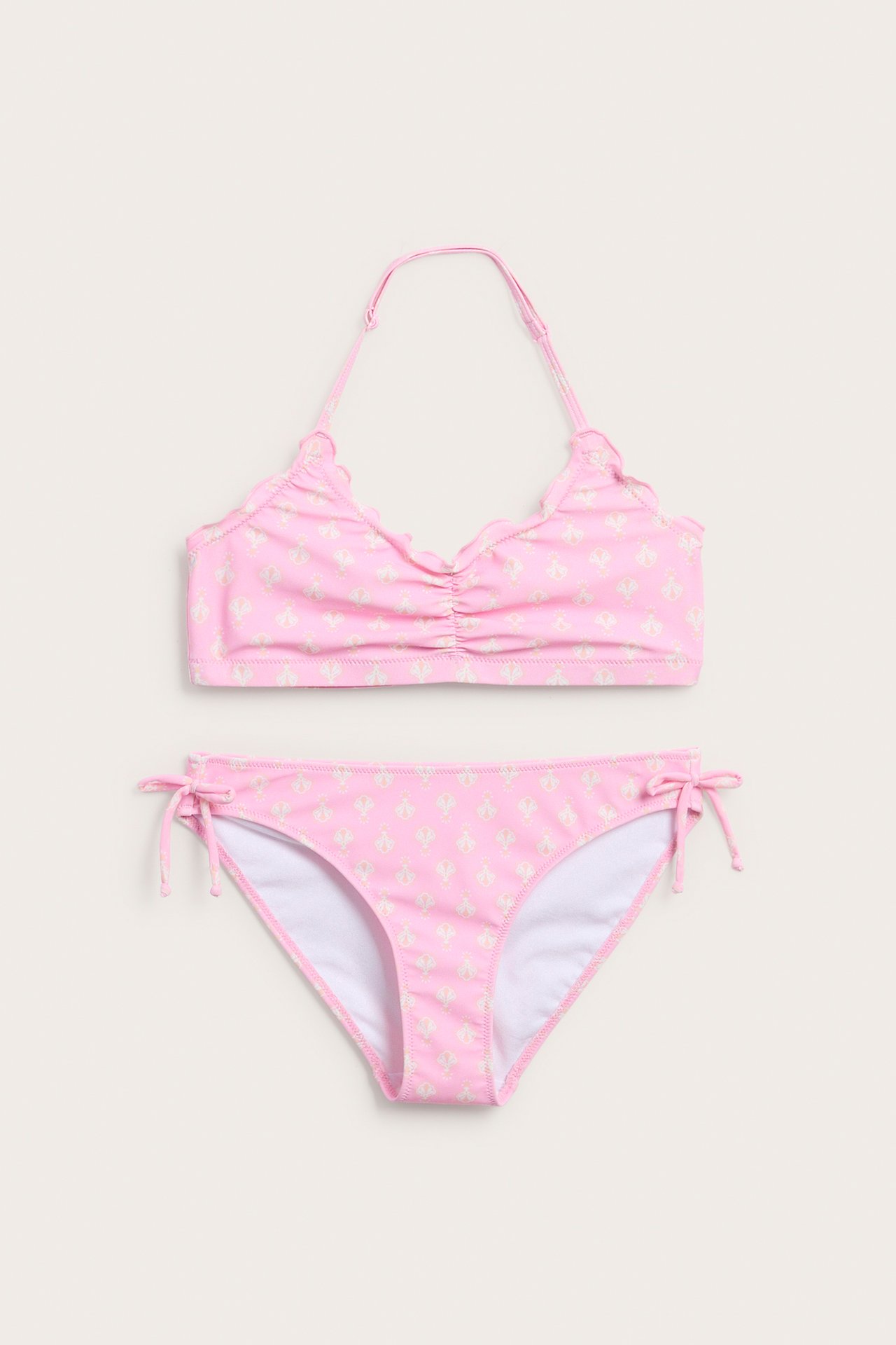 Edestä kuvattu lasten vaaleanpunainen kuviollinen halterneck-bikini, jossa on rypytetty toppi ja sidottavat alaosat.