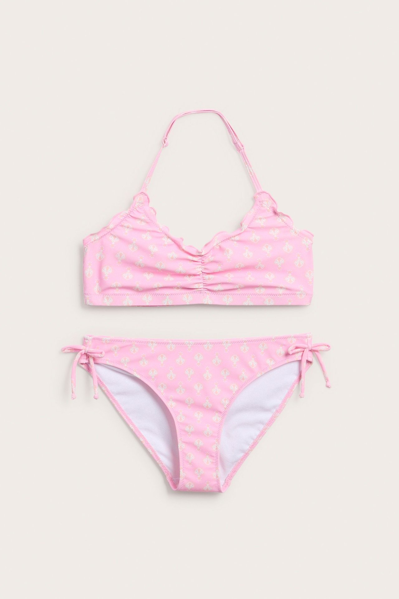 Edestä kuvattu lasten vaaleanpunainen kuviollinen halterneck-bikini, jossa on rypytetty toppi ja sidottavat alaosat.